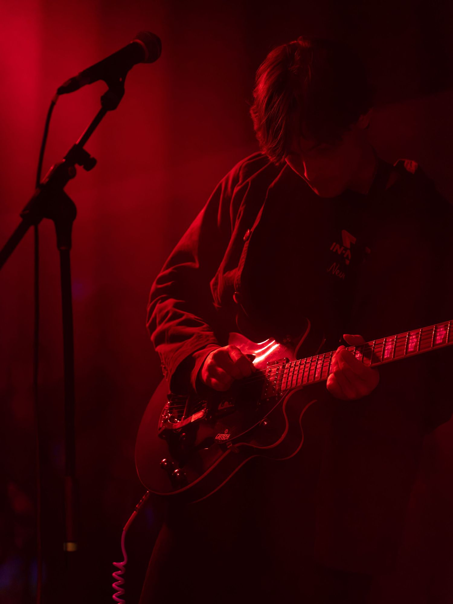 A guitarist performs on stage bathed in dramatic red lighting at a live music concert.