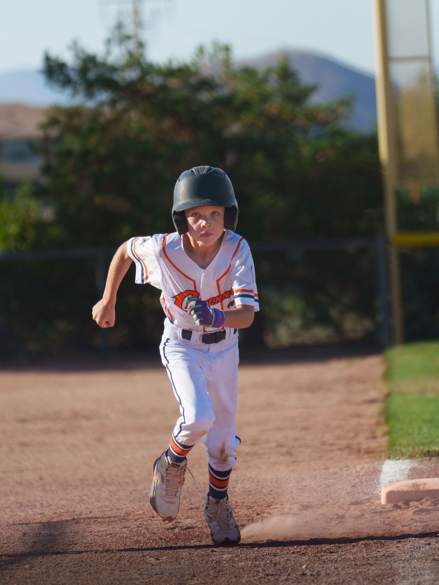 Young baseball player in white uniform sprinting the bases during a youth little league game outdoors.