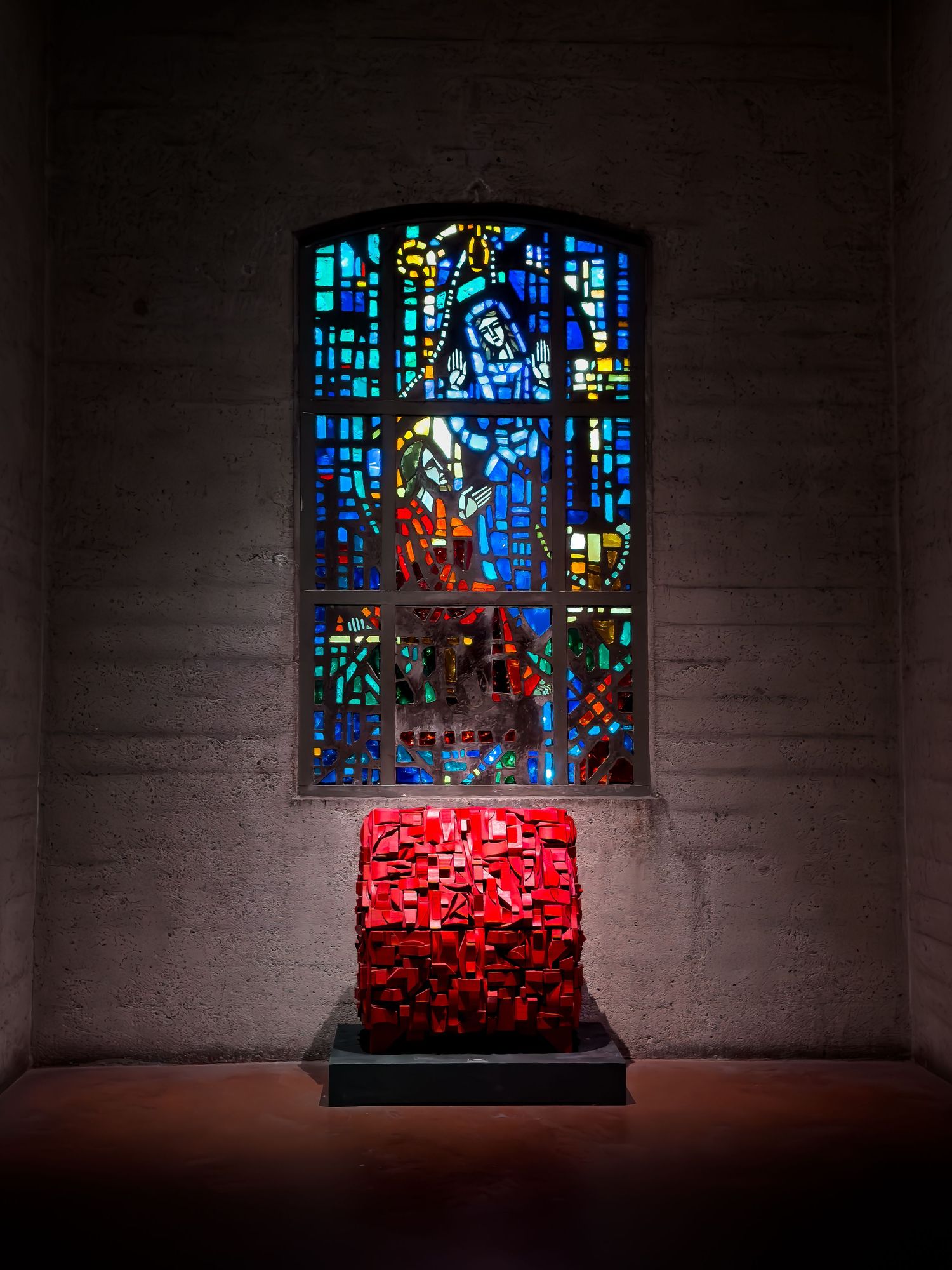 Red illuminated sculpture displayed before a colorful stained glass window inside a church.