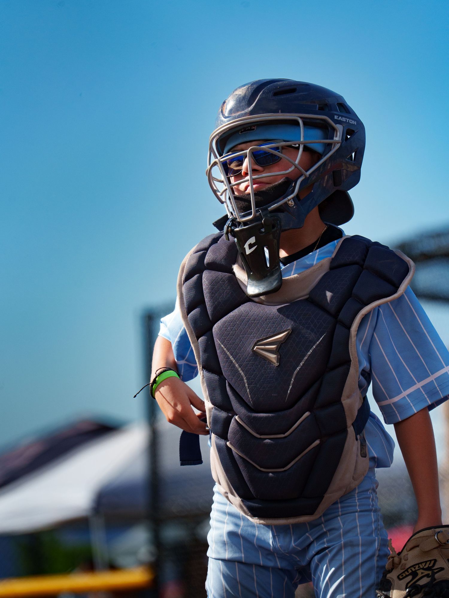 Young baseball catcher in Easton gear and helmet standing on field under clear blue sky.