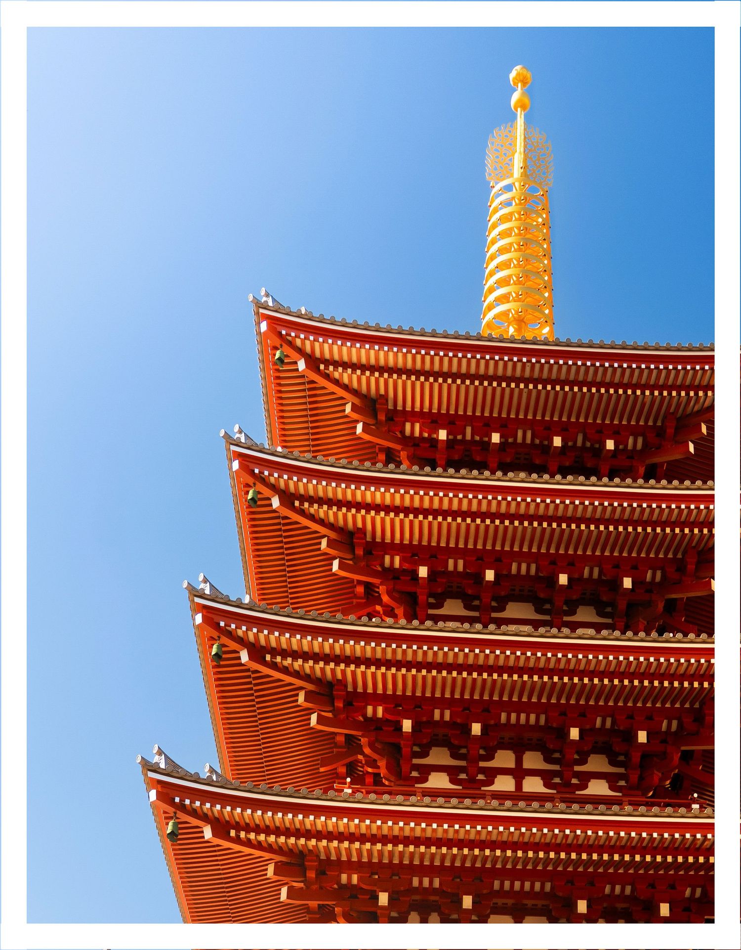 Close-up view of traditional red Japanese five-story pagoda at Senso-ji temple against clear blue sky in Tokyo.