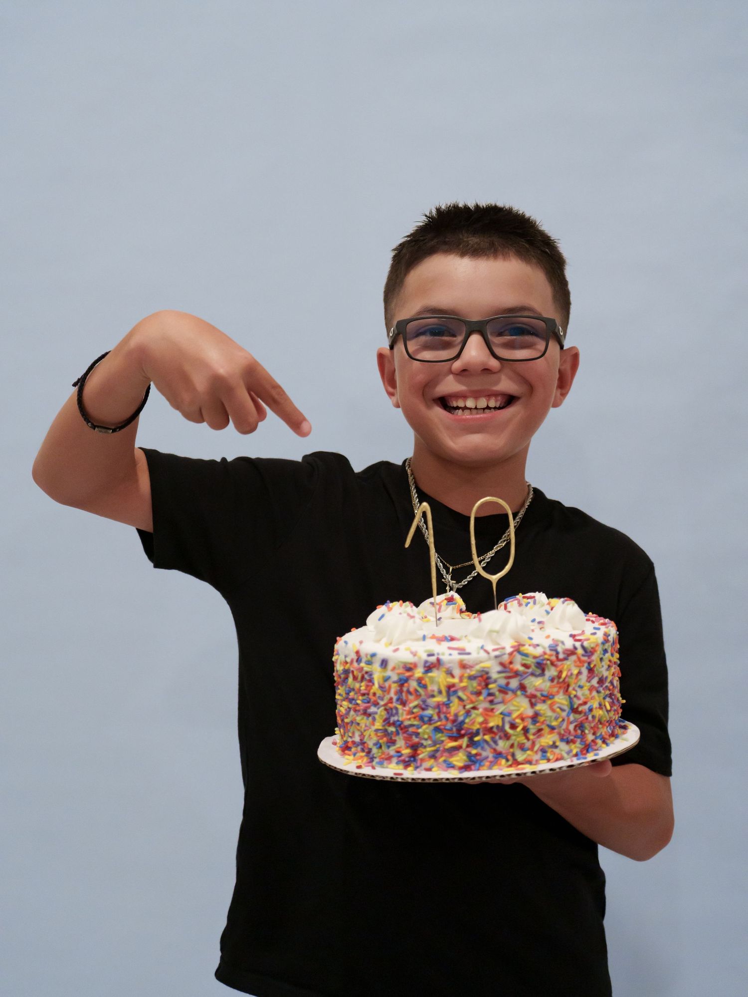 Smiling boy in black t-shirt points at colorful sprinkle birthday cake with number 10 topper.