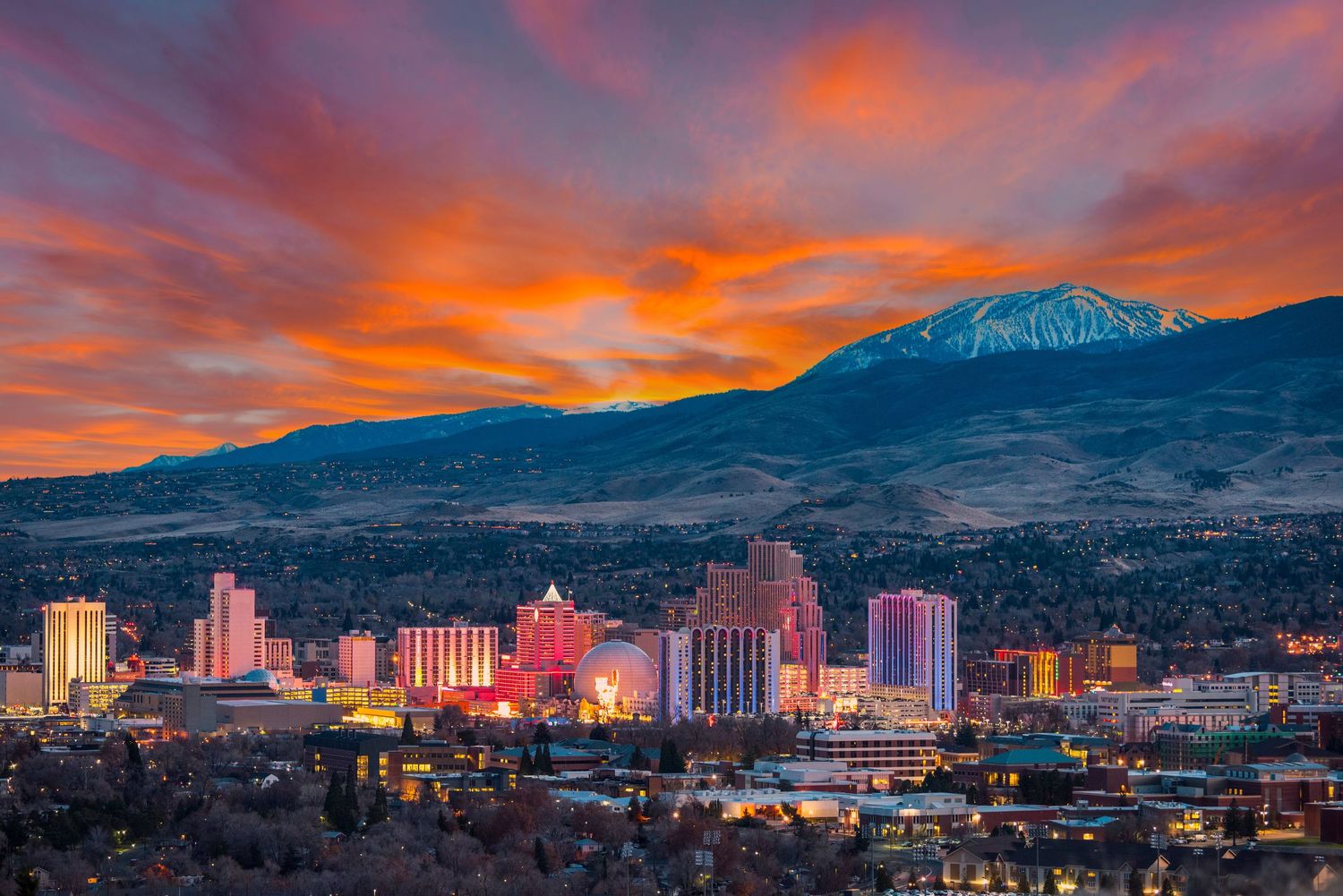 Breathtaking Reno Nevada cityscape at dusk featuring dramatic red sunset skies and snow-dusted mountain backdrop.