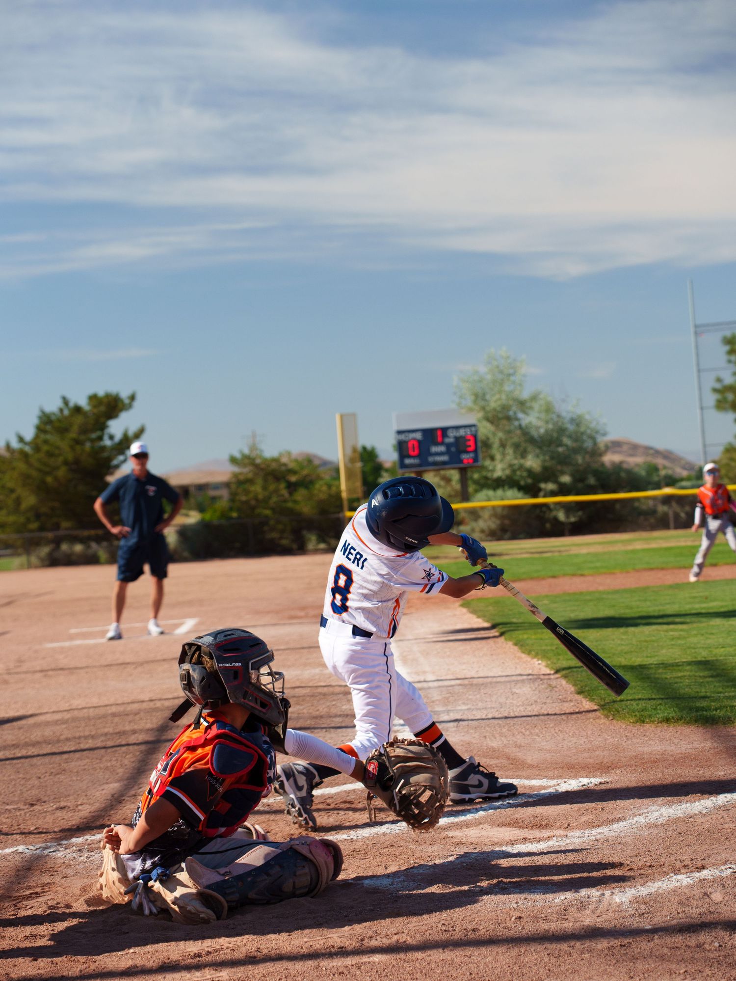 Youth baseball batter swinging at a pitch with catcher crouching behind home plate during a little league game.