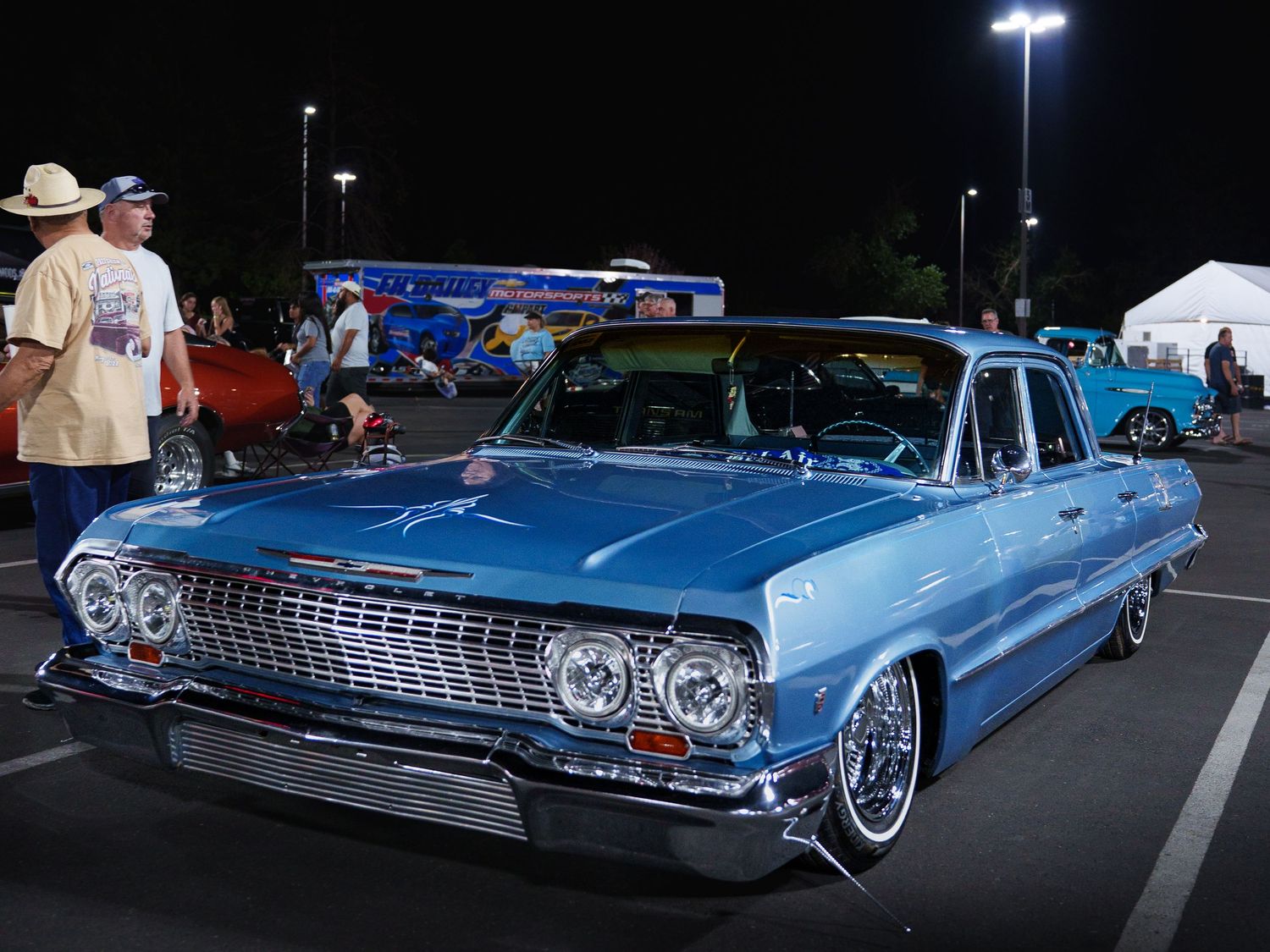 Classic blue 1963 Chevrolet Impala lowrider on display at a nighttime outdoor car show.