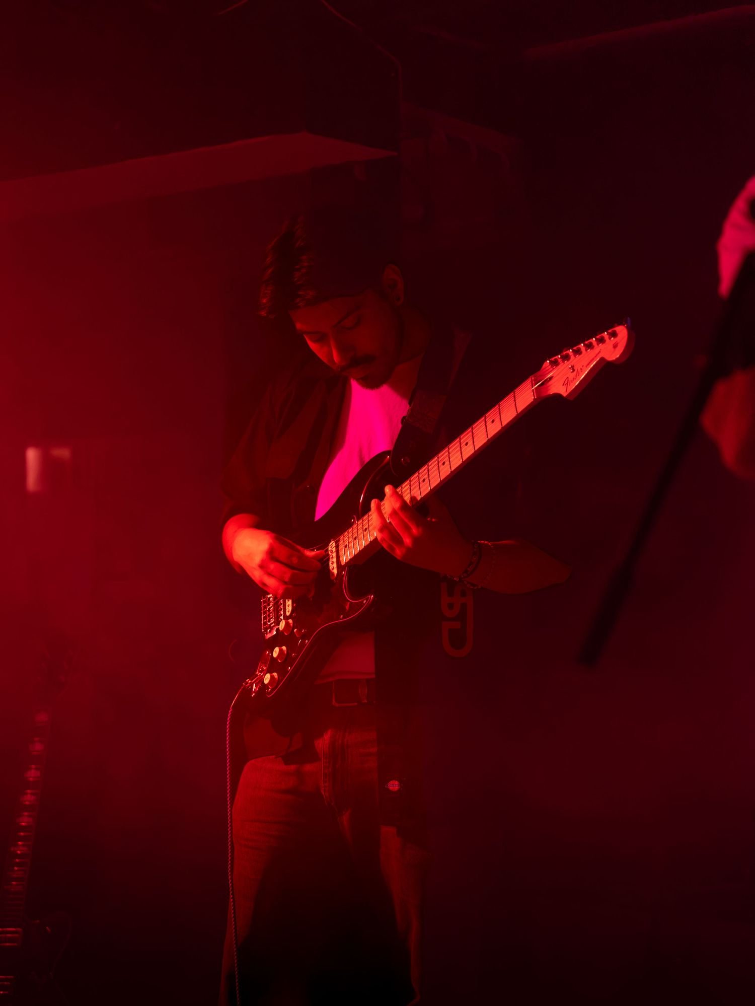 Electric guitarist performing on stage bathed in vivid red lighting during a live concert.