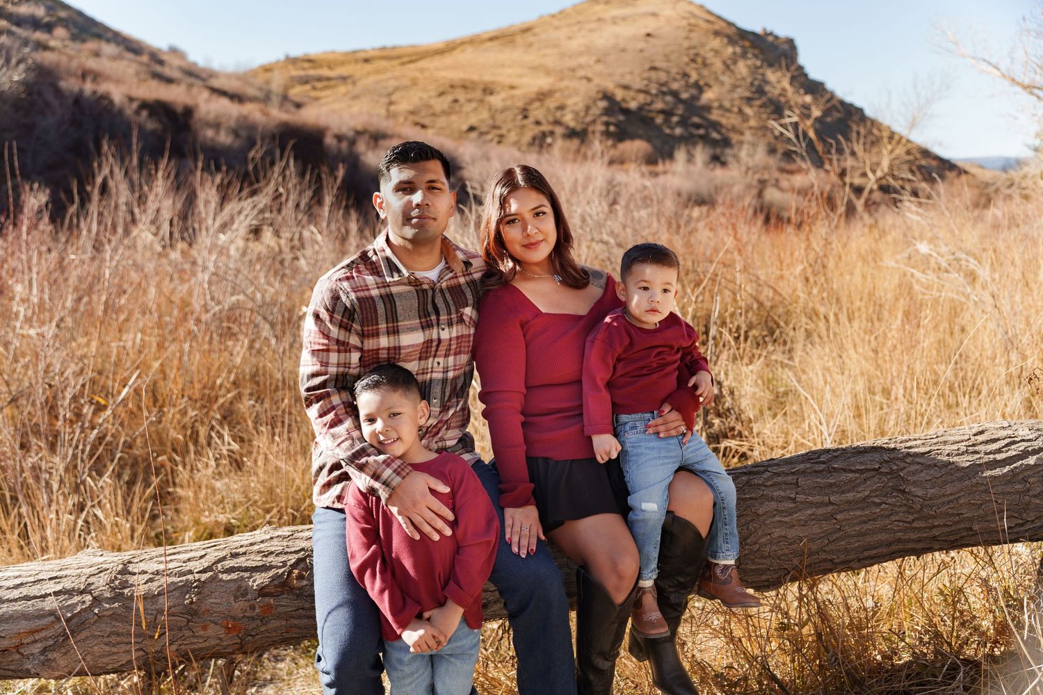 Happy Hispanic family of four posing on a fallen log in a golden autumn mountain landscape.