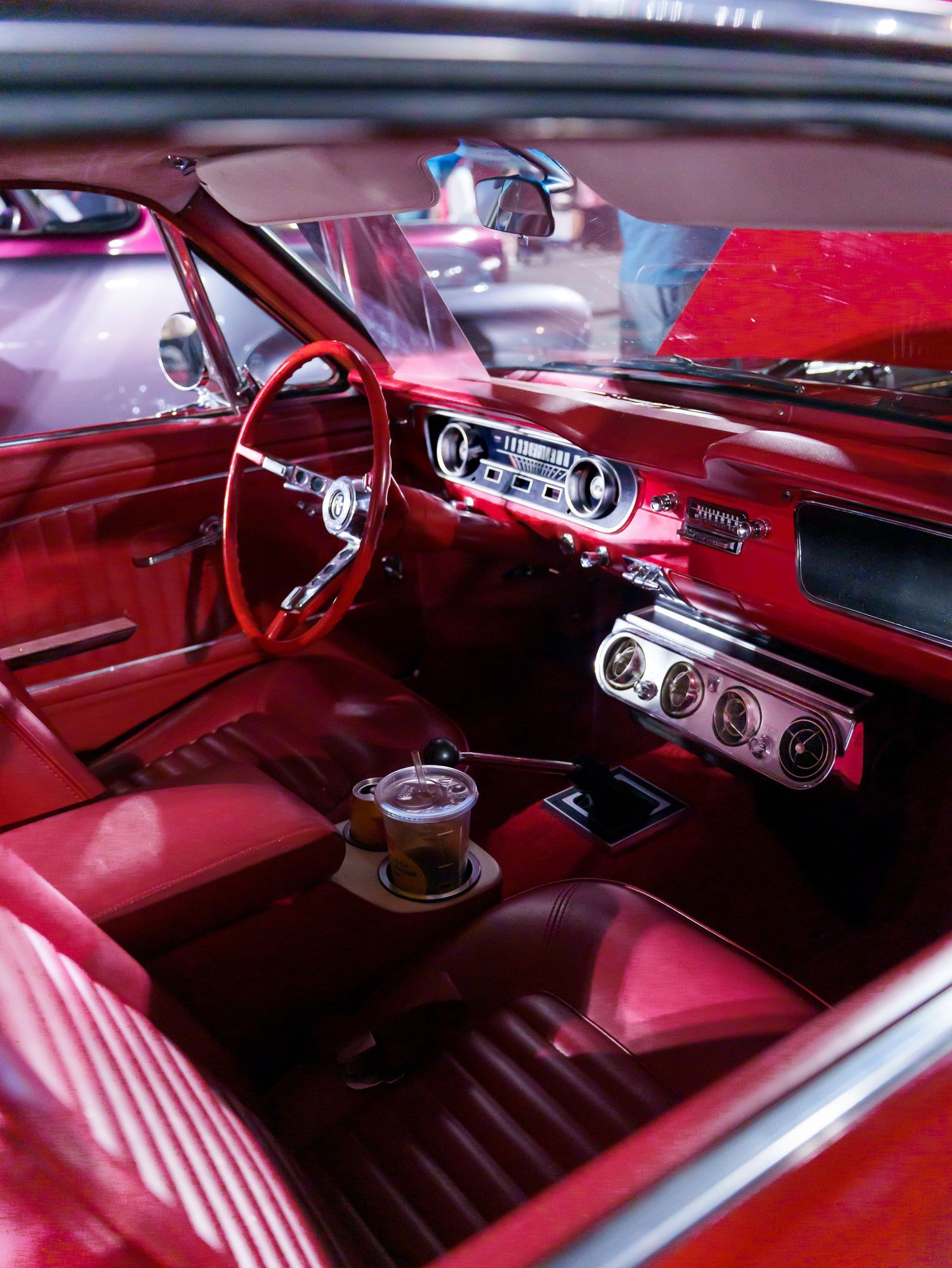 Pristine red interior of a classic Ford Mustang with matching steering wheel and dashboard at a car show.