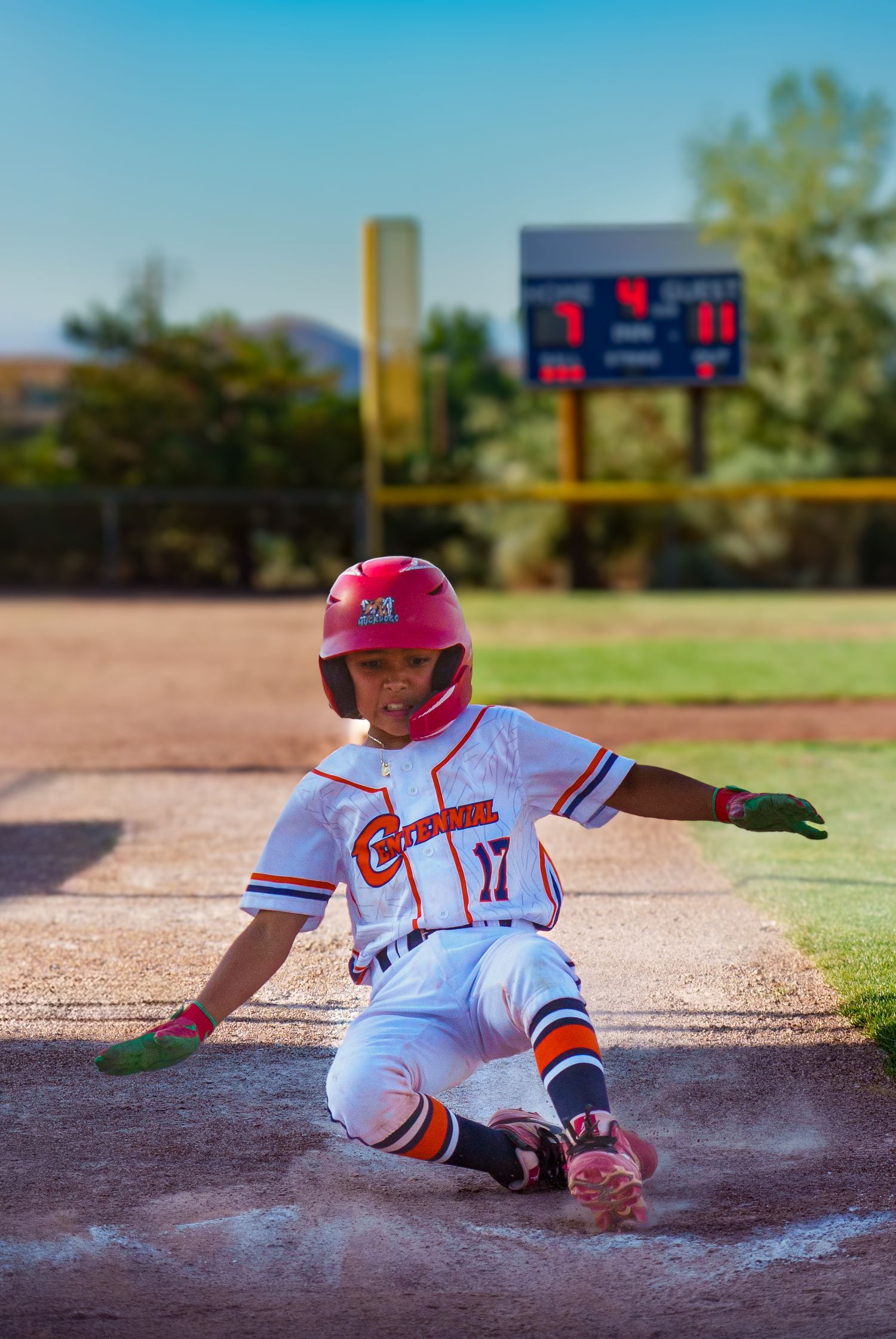 Young baseball player wearing number 17 sliding into home plate during a youth little league game.