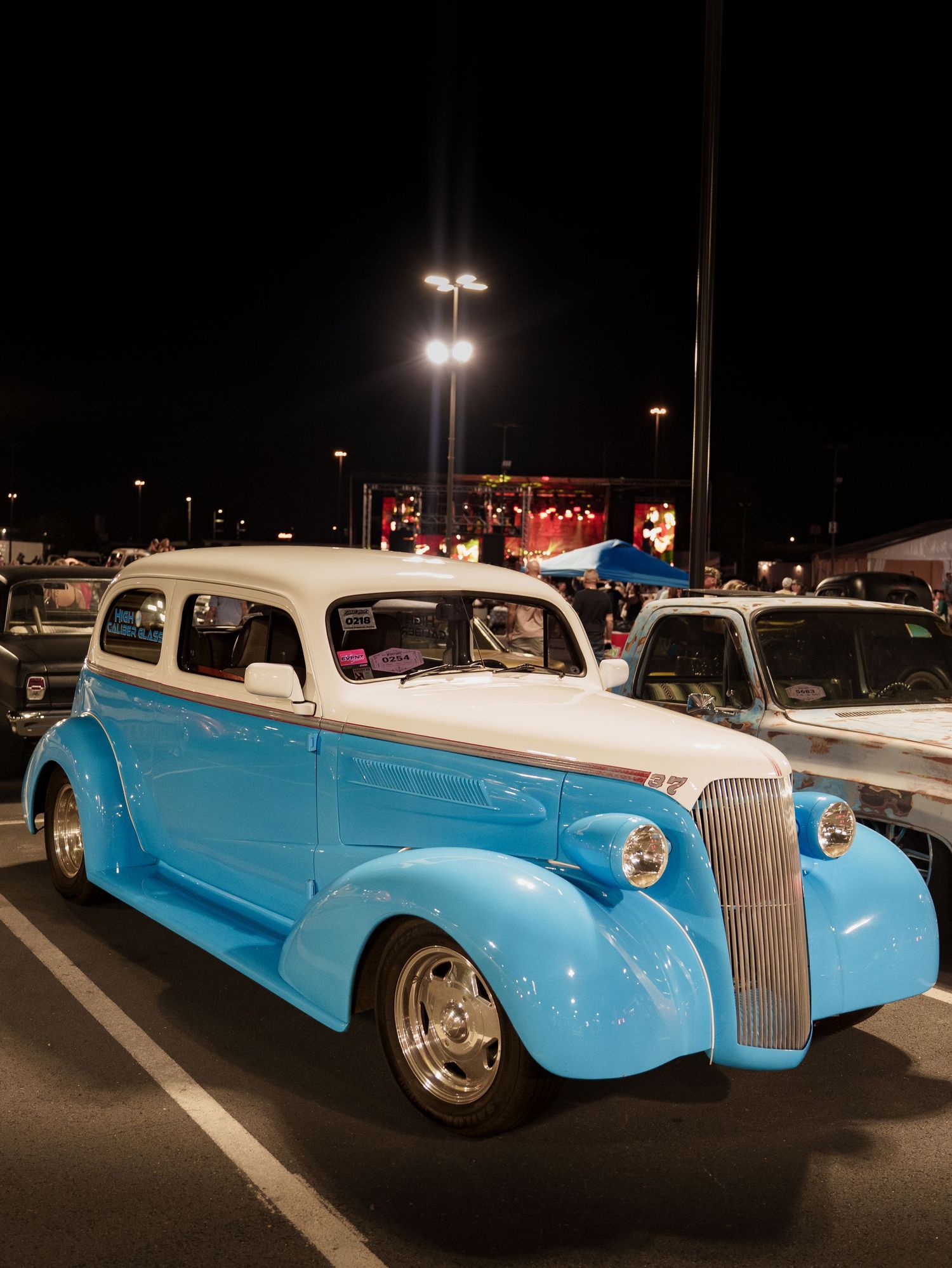 Restored blue and white 1937 Chevrolet classic car displayed at a nighttime outdoor car show.