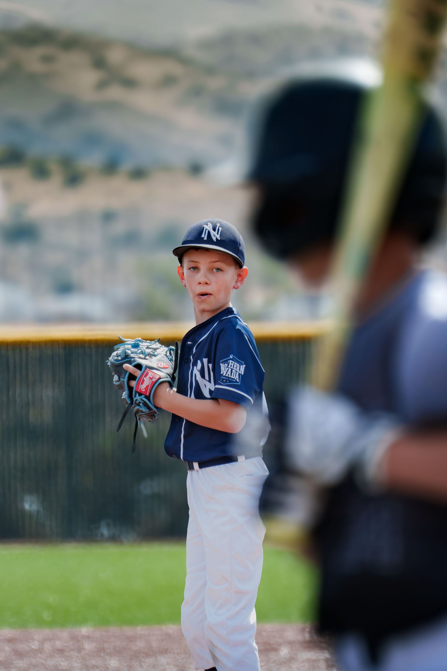 Young baseball pitcher in NY Yankees uniform holding glove ready to pitch during a youth league game.