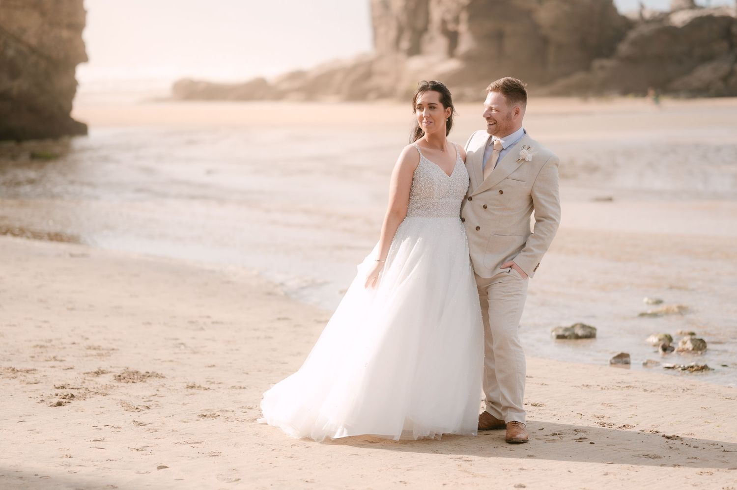 Bride and groom share a romantic moment on a sandy beach at golden hour during their wedding day.