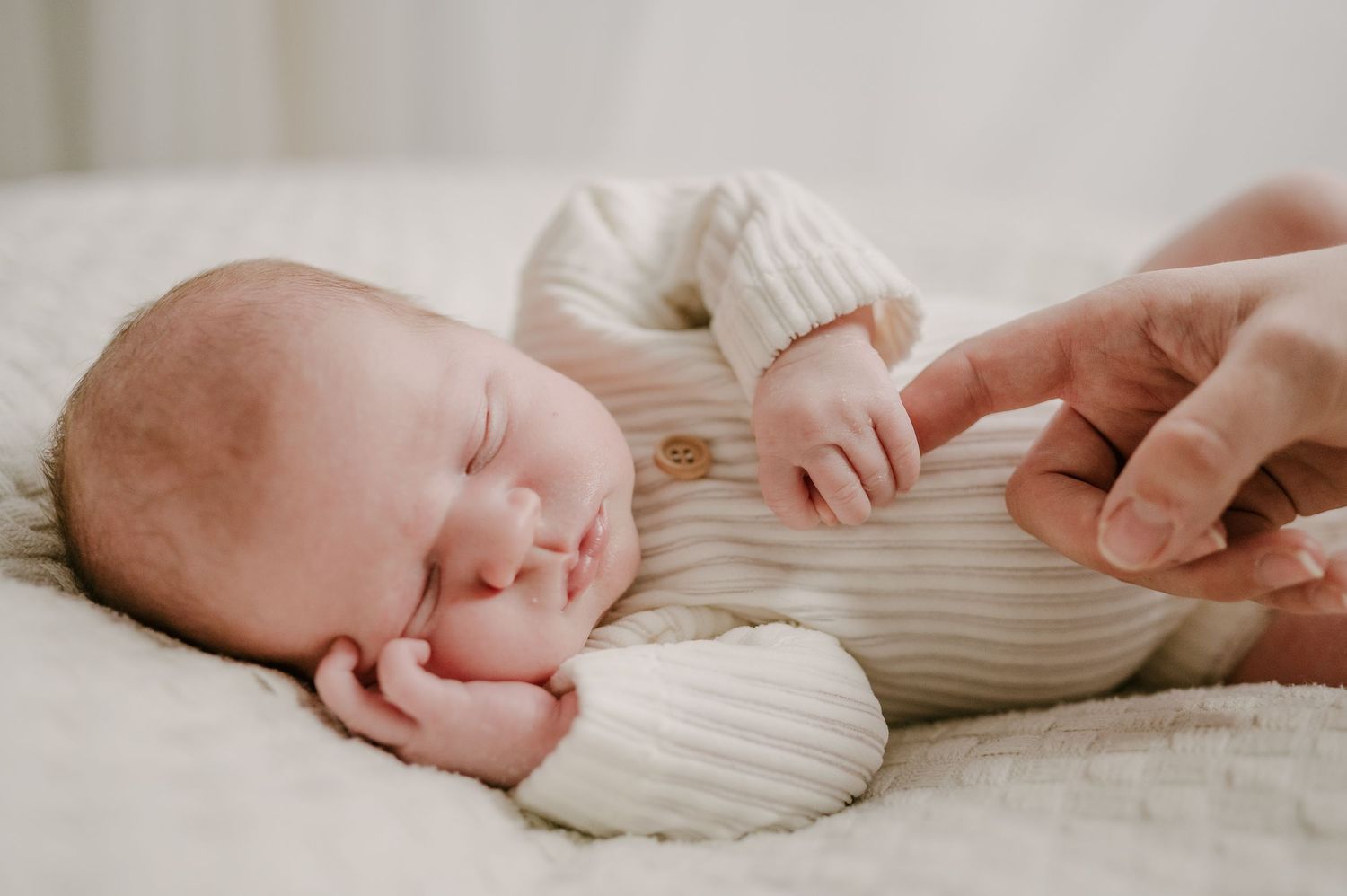 Sleeping newborn baby in striped onesie gently holding an adults finger during a newborn photo session.