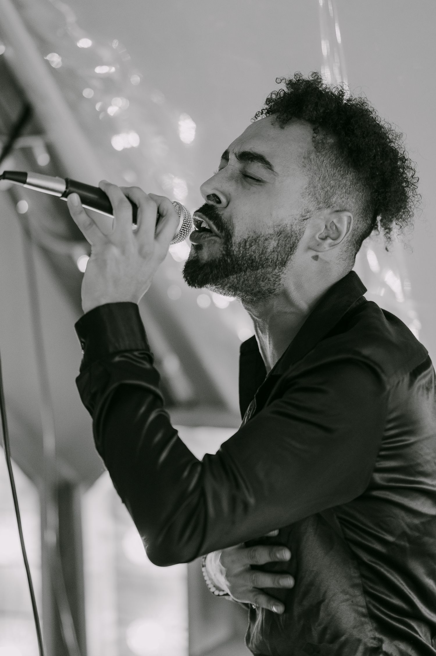 Black and white close-up of male wedding singer performing passionately with microphone on stage.