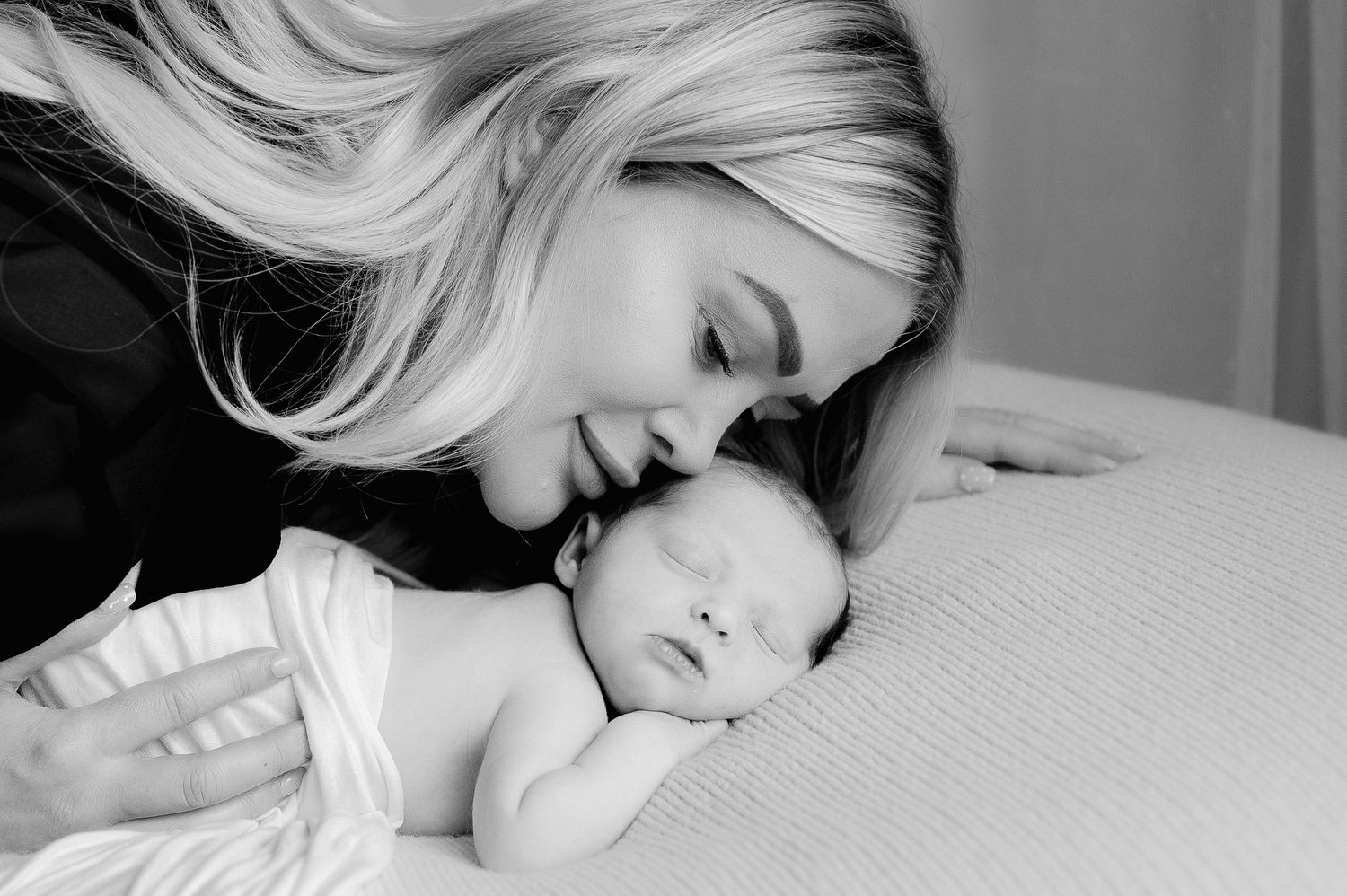 Black and white photo of a blonde mother lovingly kissing her newborn baby's head.