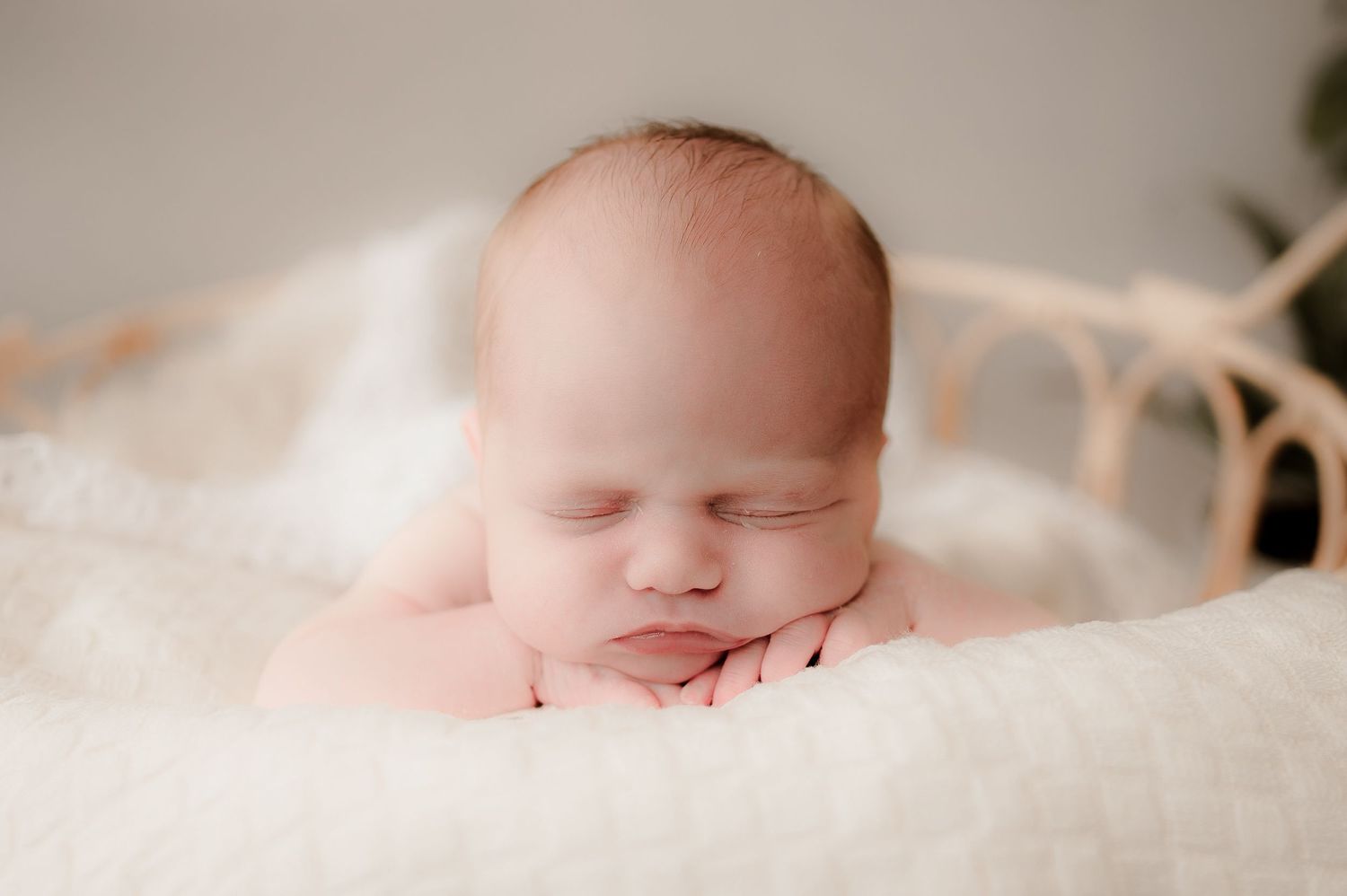Peaceful newborn baby sleeping with hands under chin in a cozy wicker basket with white fur.
