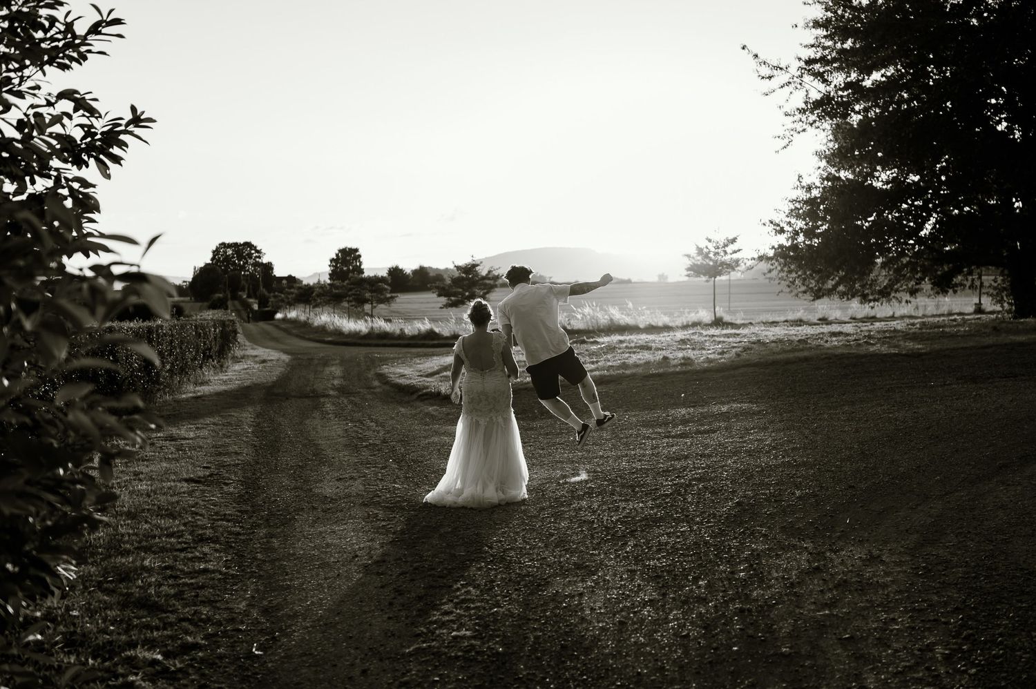 Black and white photo of bride and groom walking down a rural dirt road on their wedding day.