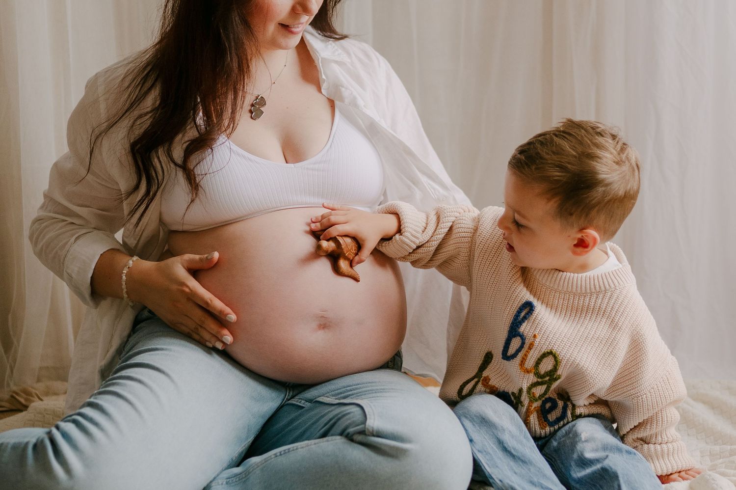 Young boy playfully touching his pregnant mothers bare baby bump during a maternity photo session.