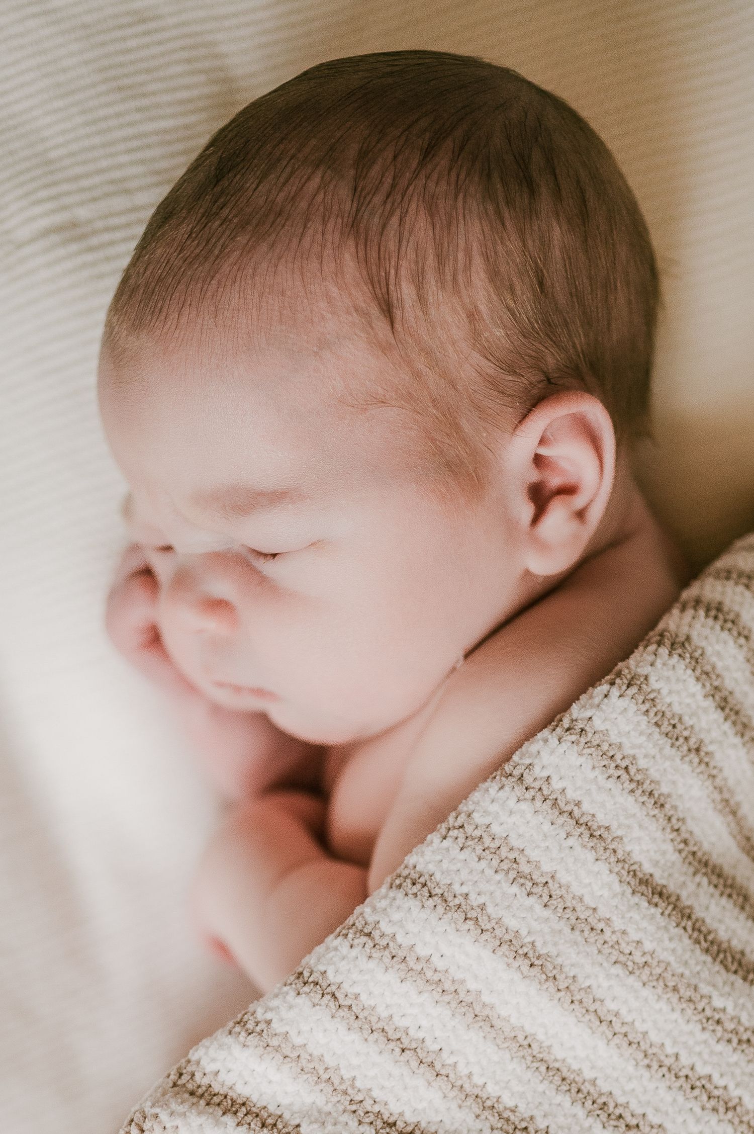 Close-up profile portrait of a sleeping newborn baby wrapped in a striped knit blanket.