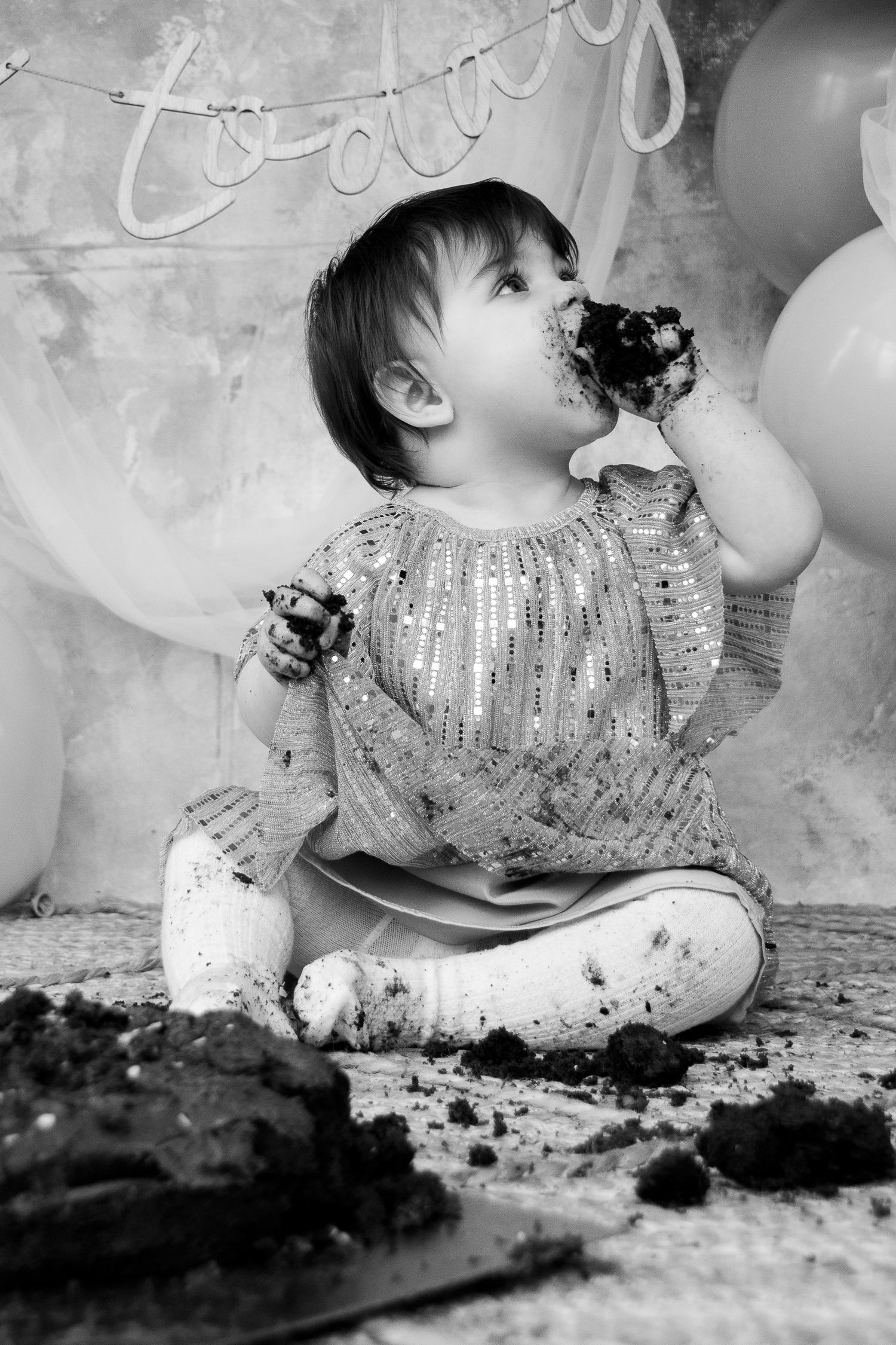 Black and white photo of baby enjoying first birthday cake smash celebration.