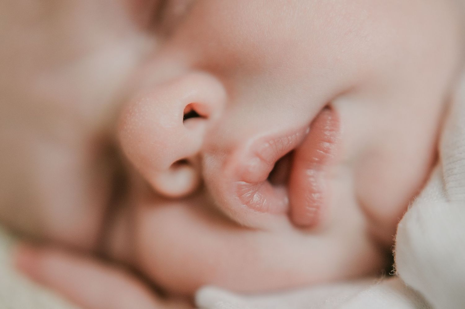 Extreme close-up macro photo of a sleeping newborn baby's nose, lips, and tiny fingers.