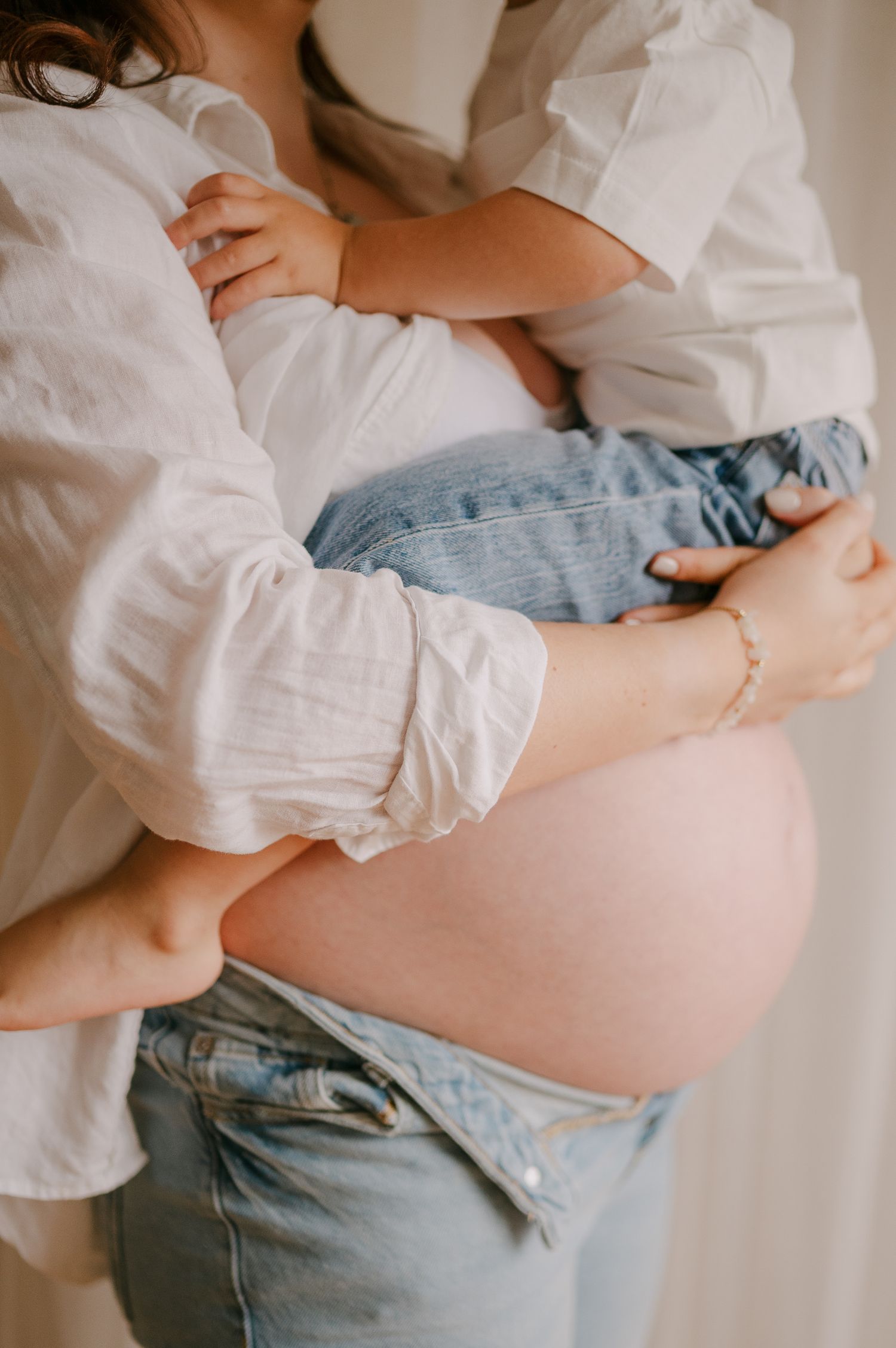 Pregnant woman in white shirt and jeans holding a young child against her bare baby bump.