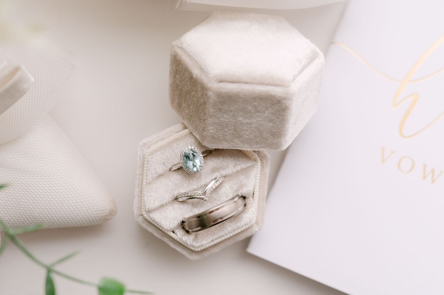 Wedding rings and aquamarine engagement ring displayed in a velvet hexagonal ring box on a white surface.