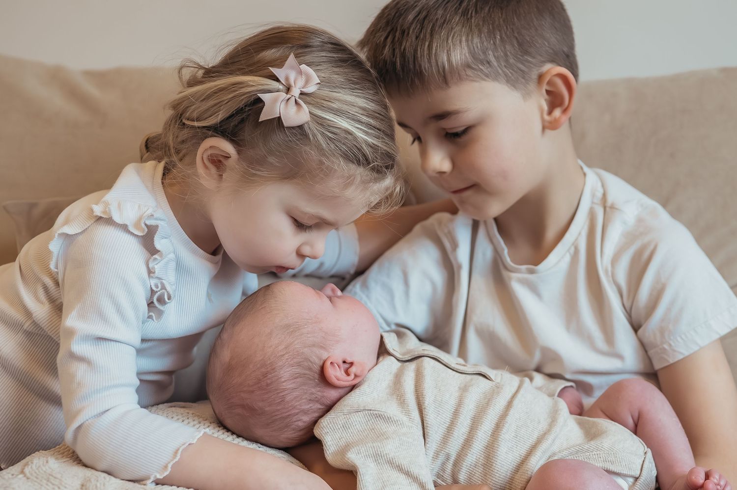 Two young siblings lovingly gazing at newborn baby during professional newborn family portrait session.