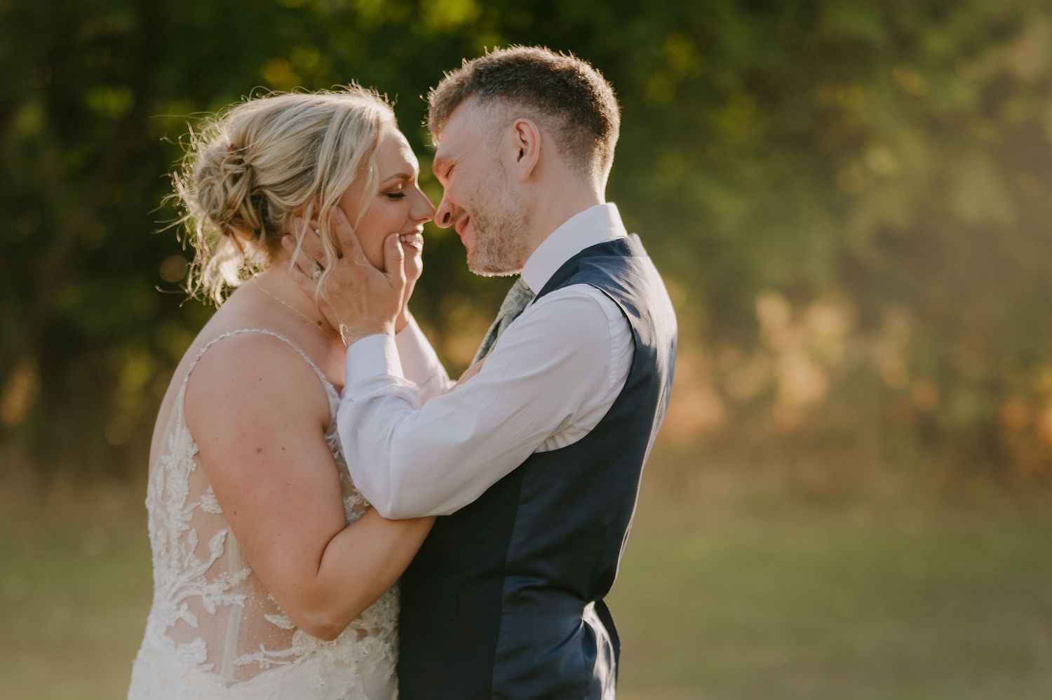 Bride and groom share a tender almost-kiss in golden sunlight during their outdoor wedding celebration.