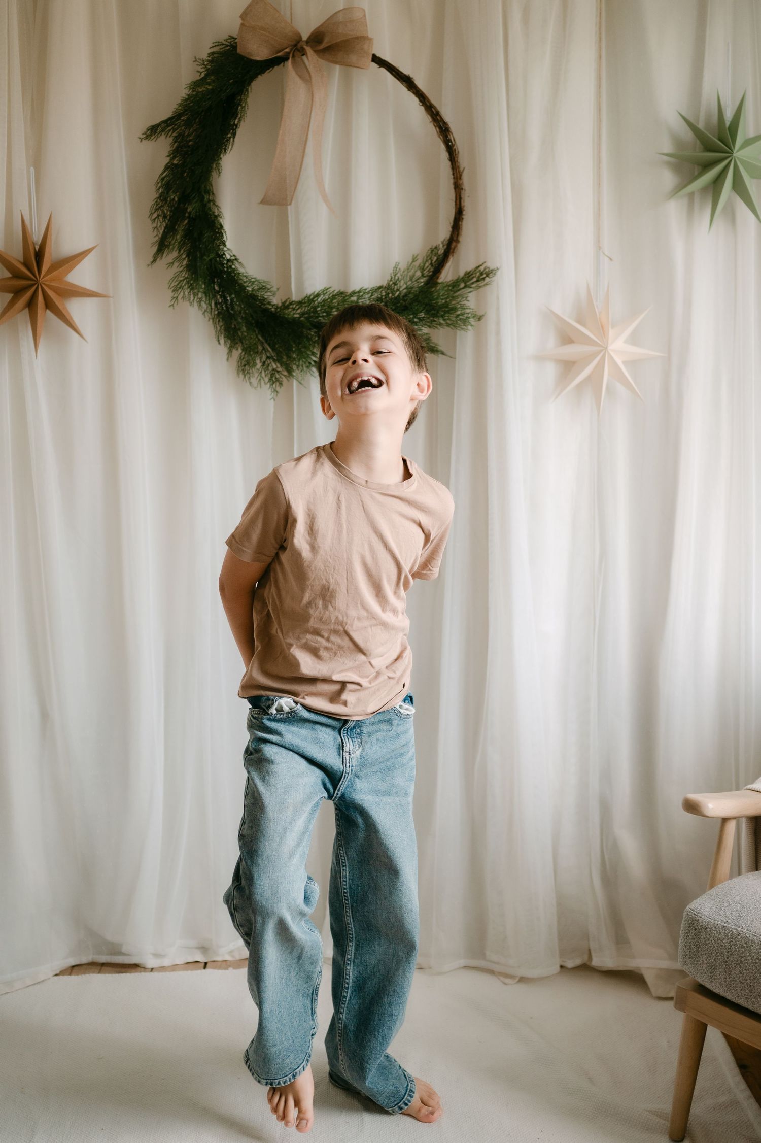 Joyful boy laughing in front of festive holiday backdrop with green wreath and paper stars decorations.
