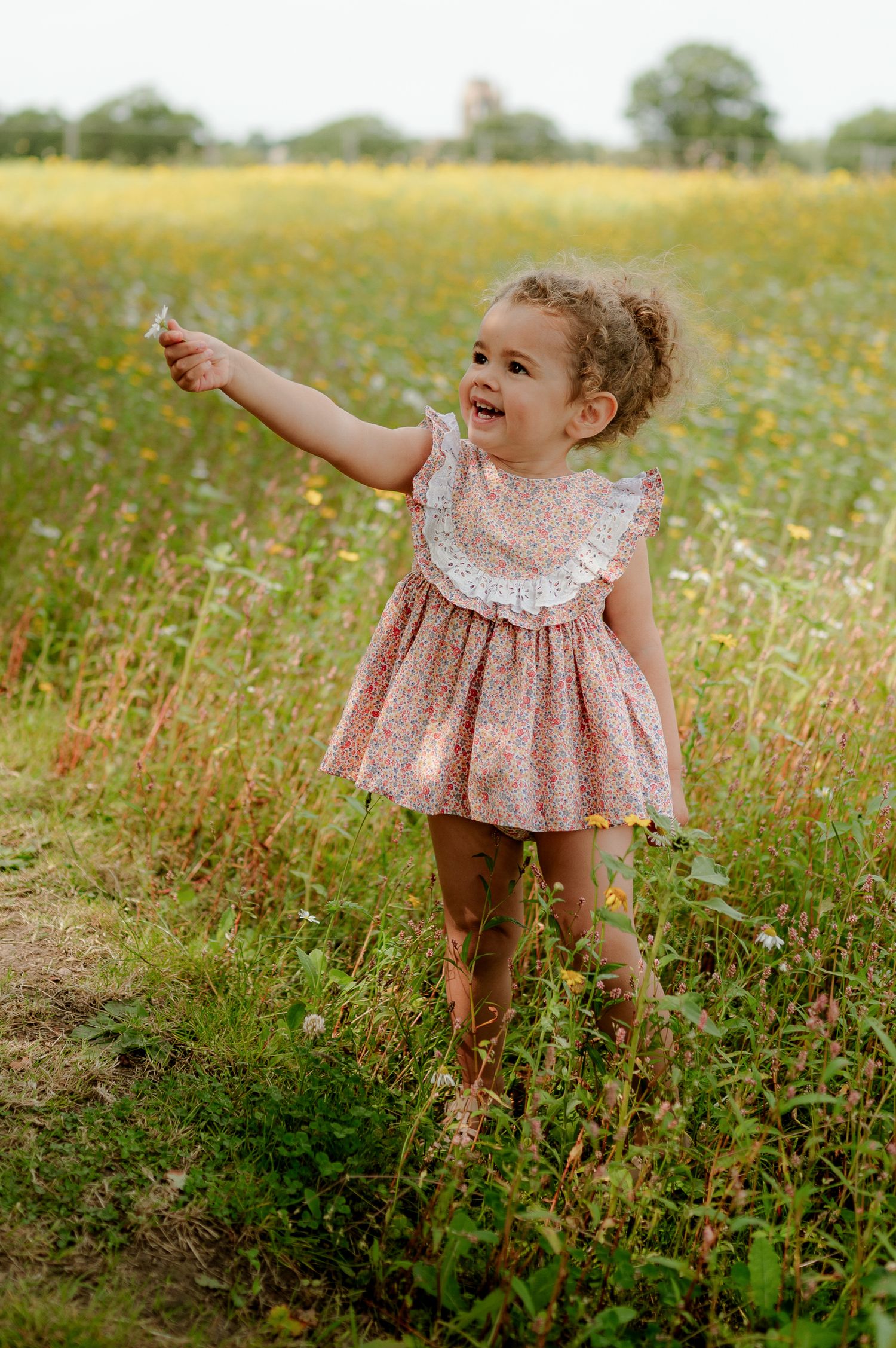 Toddler girl in floral pink dress reaching out in a wildflower meadow.