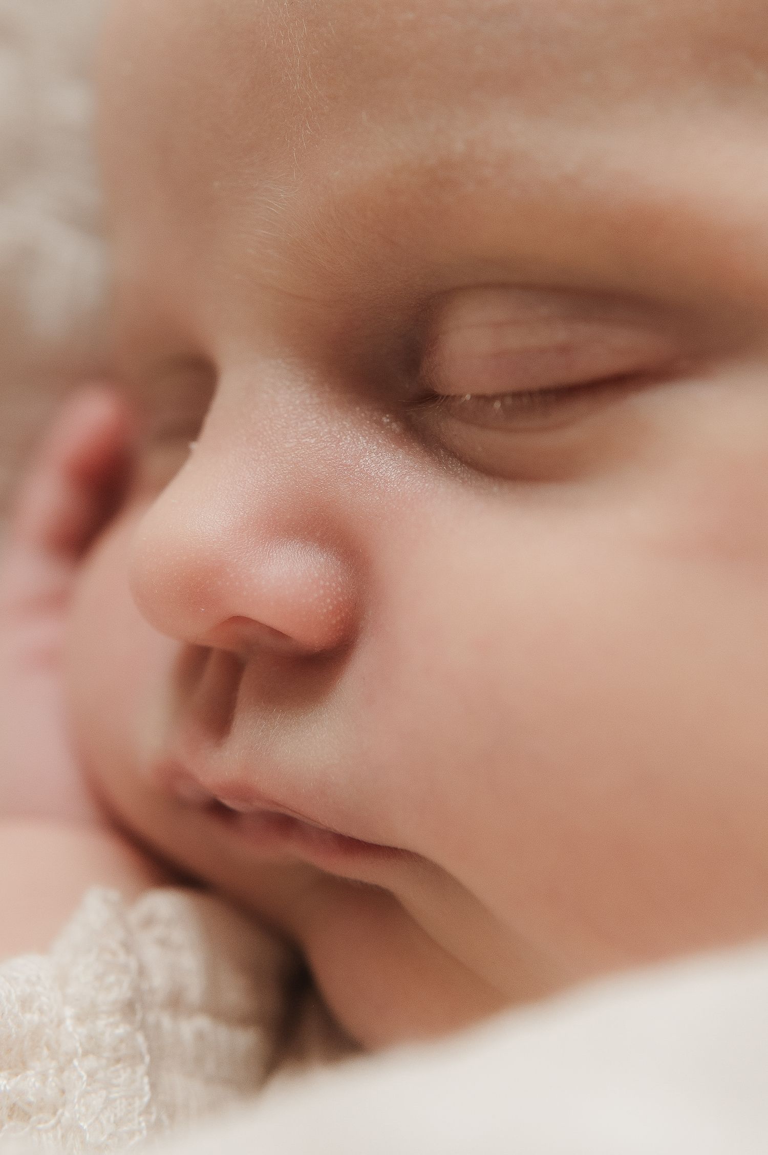 Extreme close-up of a sleeping newborn baby's serene face resting on soft white fabric.