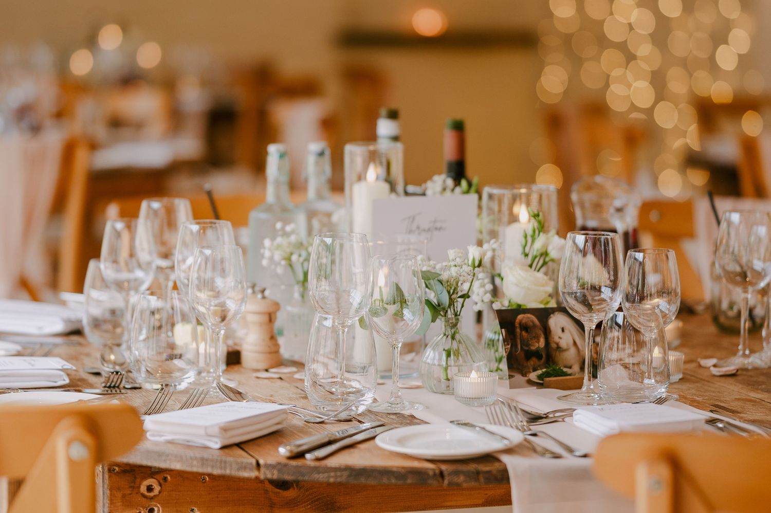 Elegant wedding reception table set with white flowers, candles, glassware, and wooden chairs.