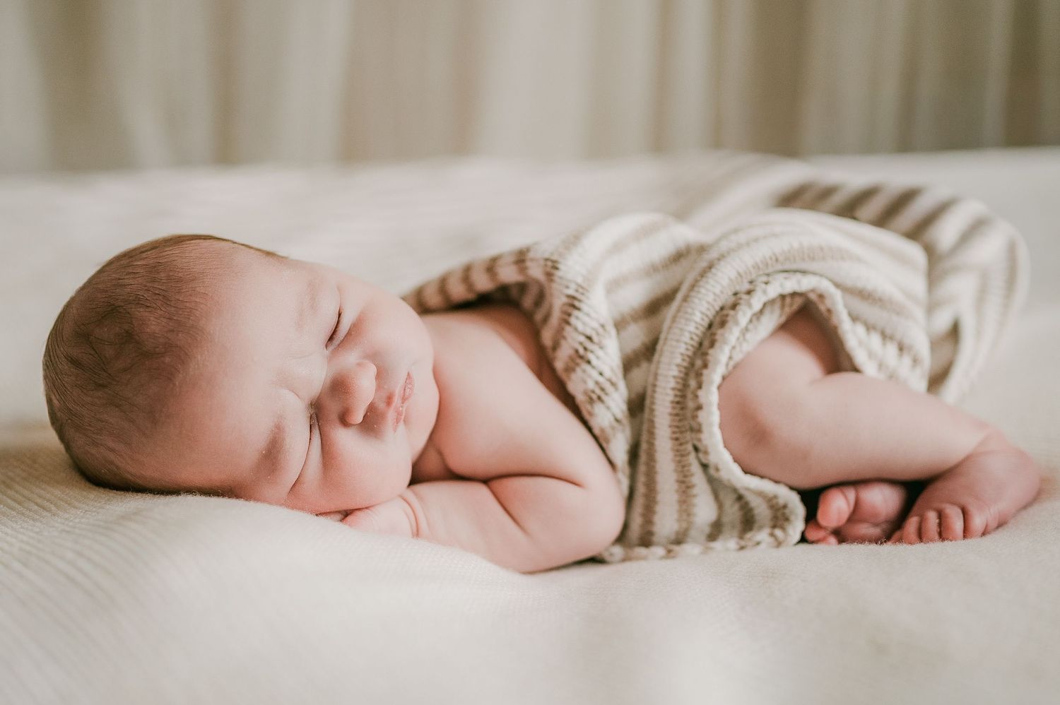Peaceful newborn baby sleeping curled up in a striped knit romper on a white surface.