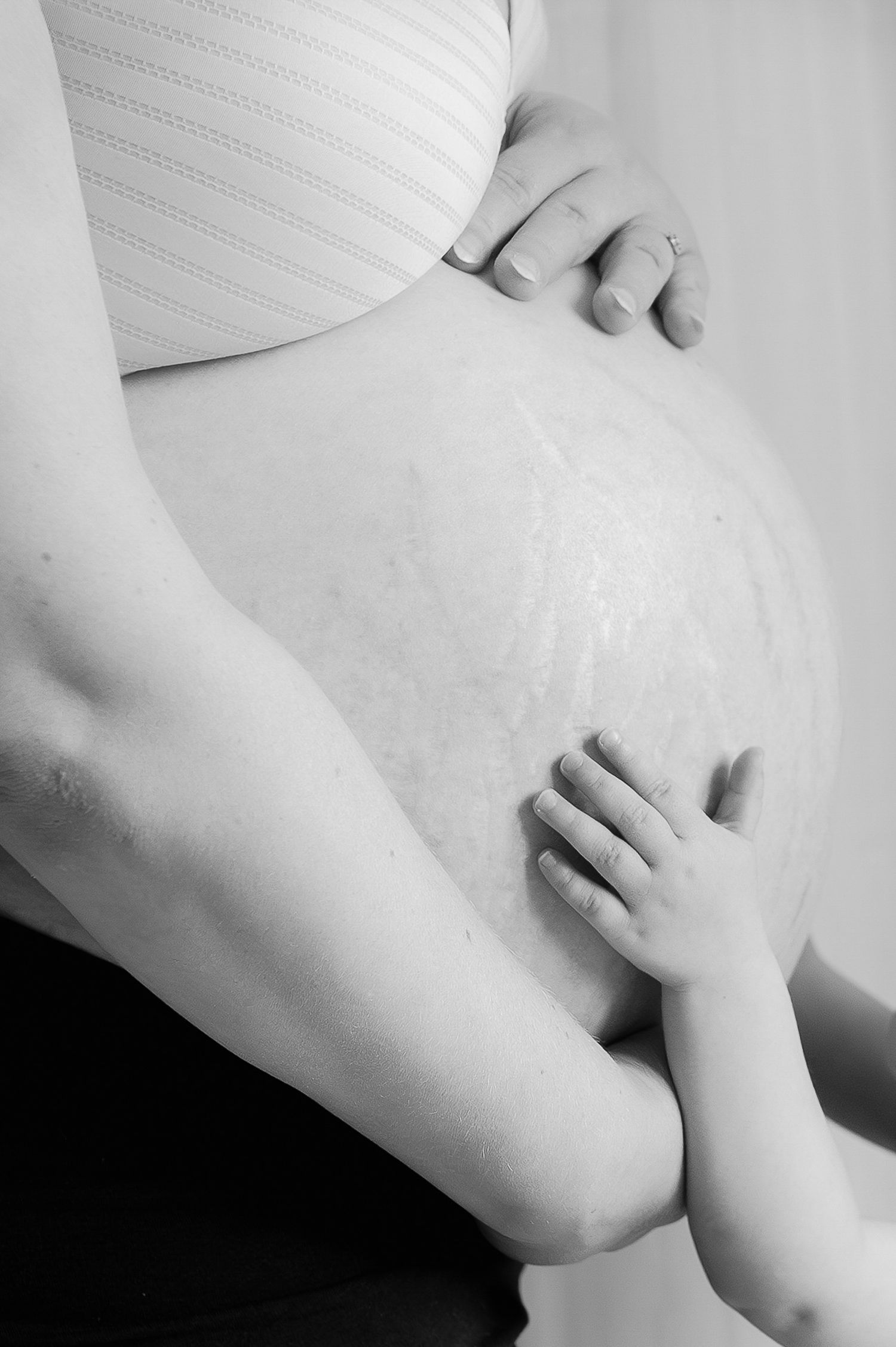 Black and white image of child touching pregnant mothers bare baby bump tenderly.