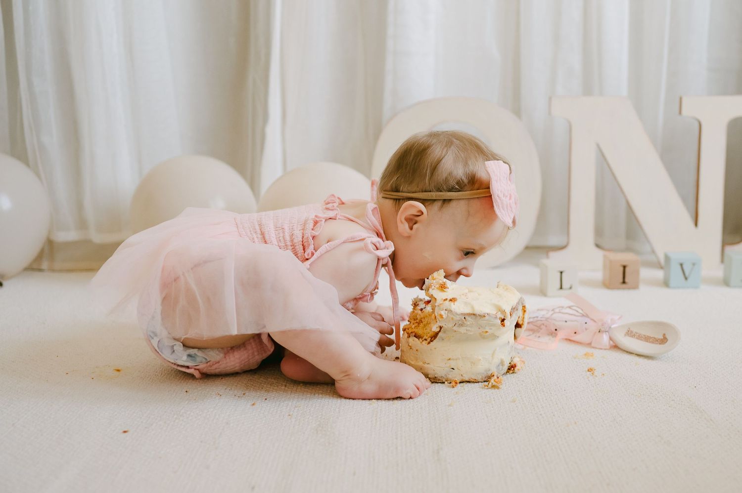Baby girl in pink tutu smashing her first birthday cake on a white floor during cake smash session.