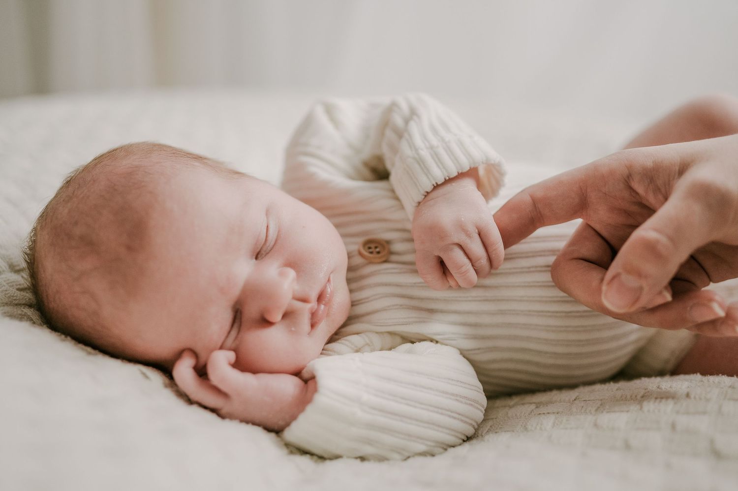 Newborn baby sleeping peacefully while adult gently holds tiny fingers.