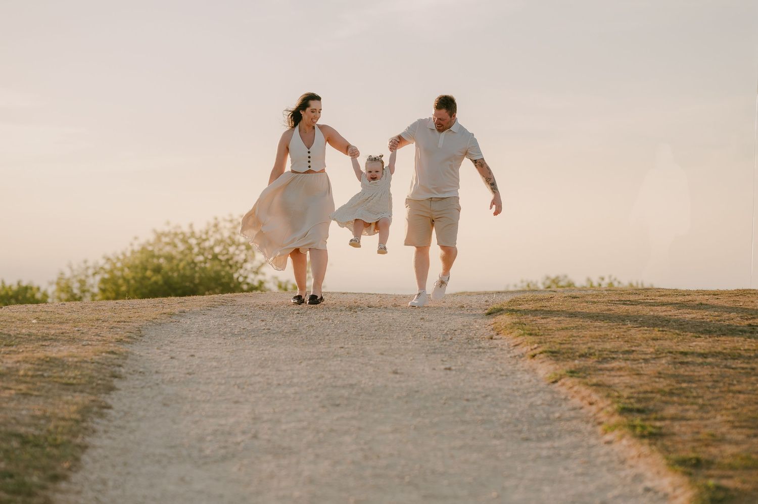 Happy family swinging young child between them on a sunny outdoor pathway.
