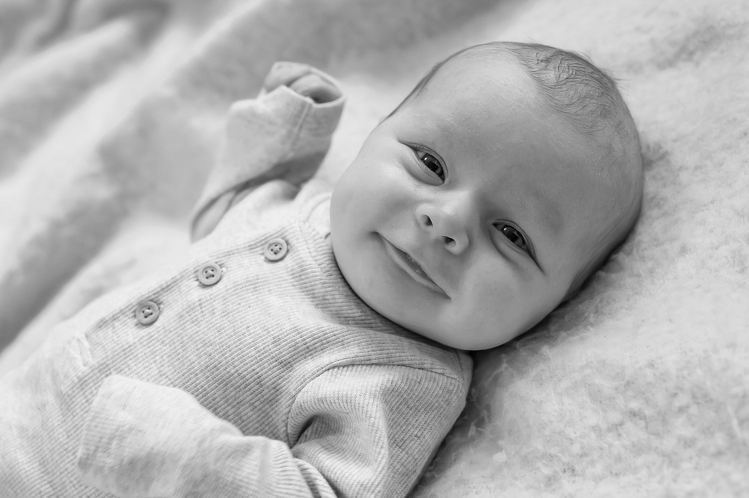 Black and white portrait of smiling alert newborn baby lying on blanket.