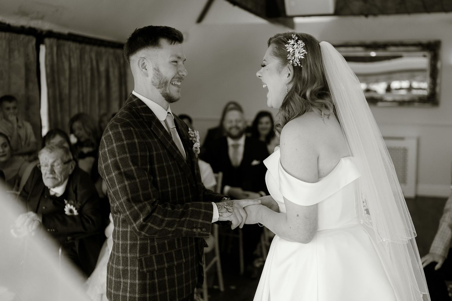 Black and white photo of smiling bride and groom exchanging vows at wedding ceremony altar.