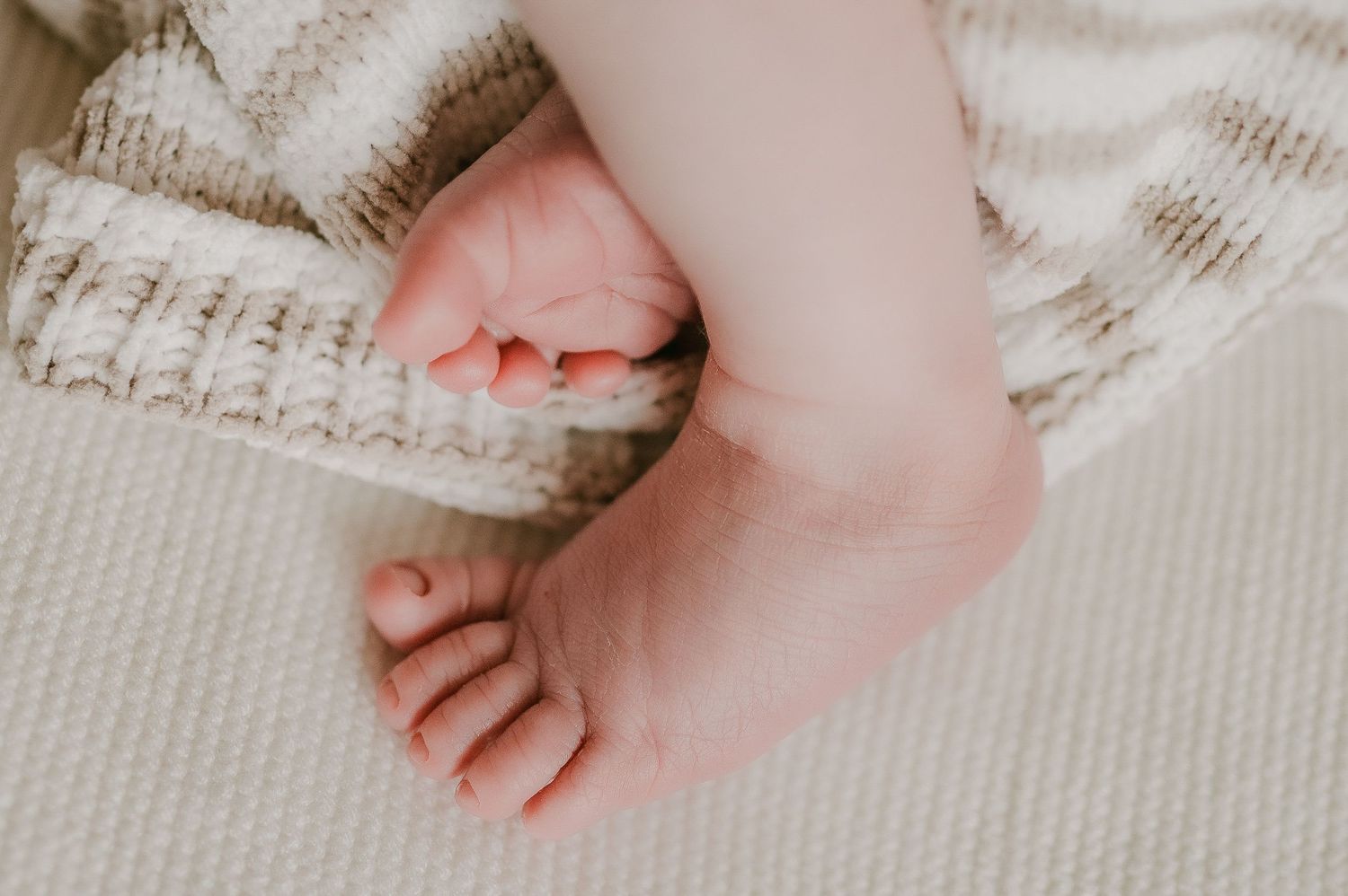 Close-up of a sleeping newborn baby's tiny feet wrapped in a soft knitted blanket.
