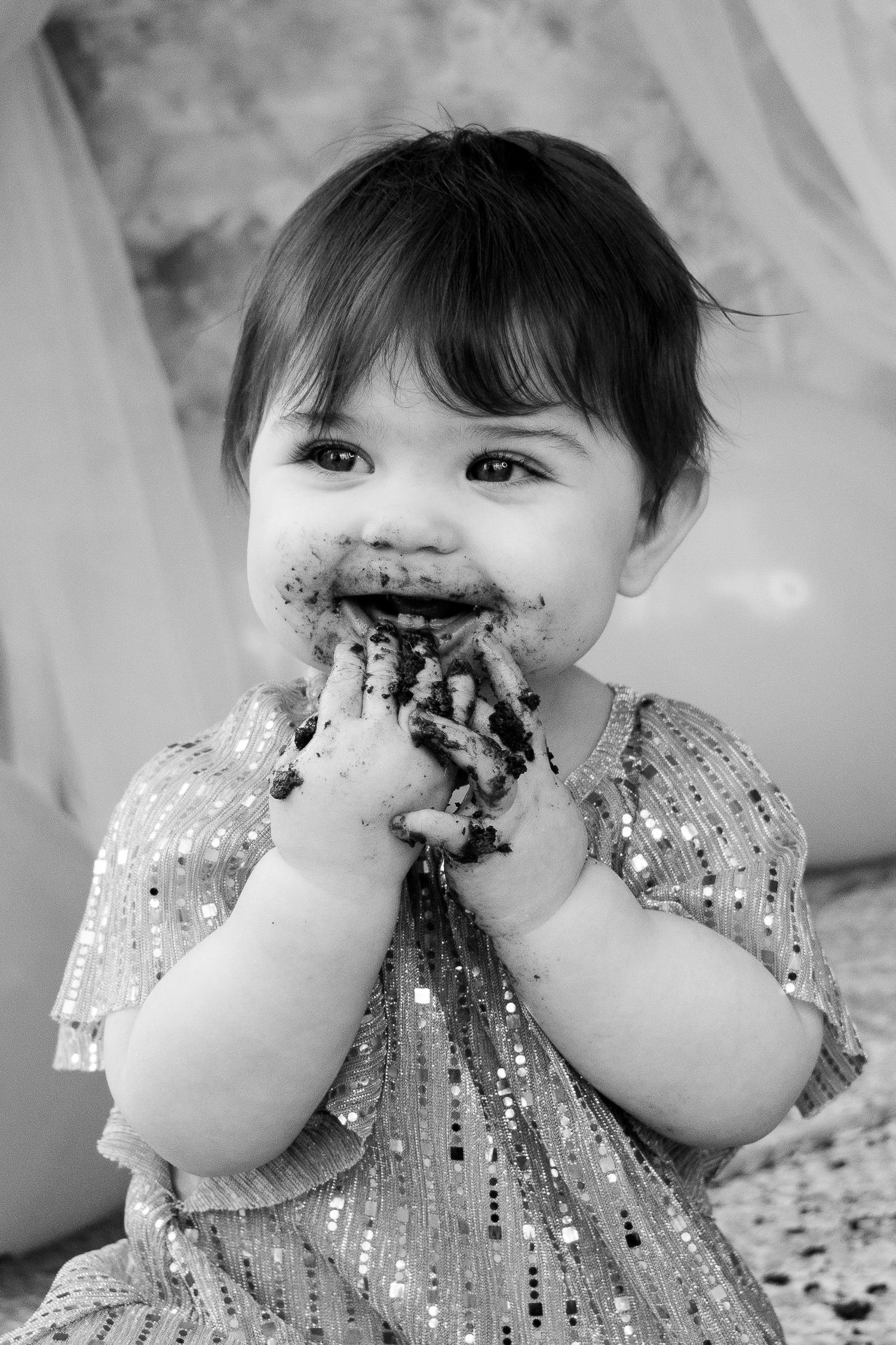 Black and white portrait of a baby girl with cake-covered hands and face during cake smash session.