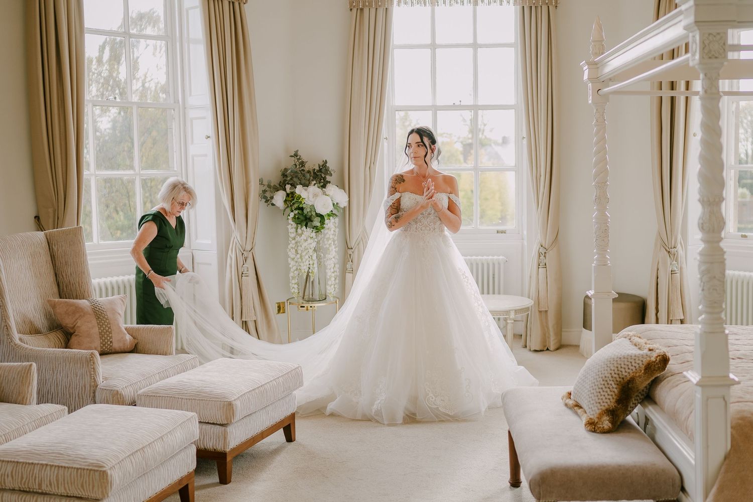 Bride in a ball gown wedding dress getting ready in an elegant room while a bridesmaid arranges her long train.