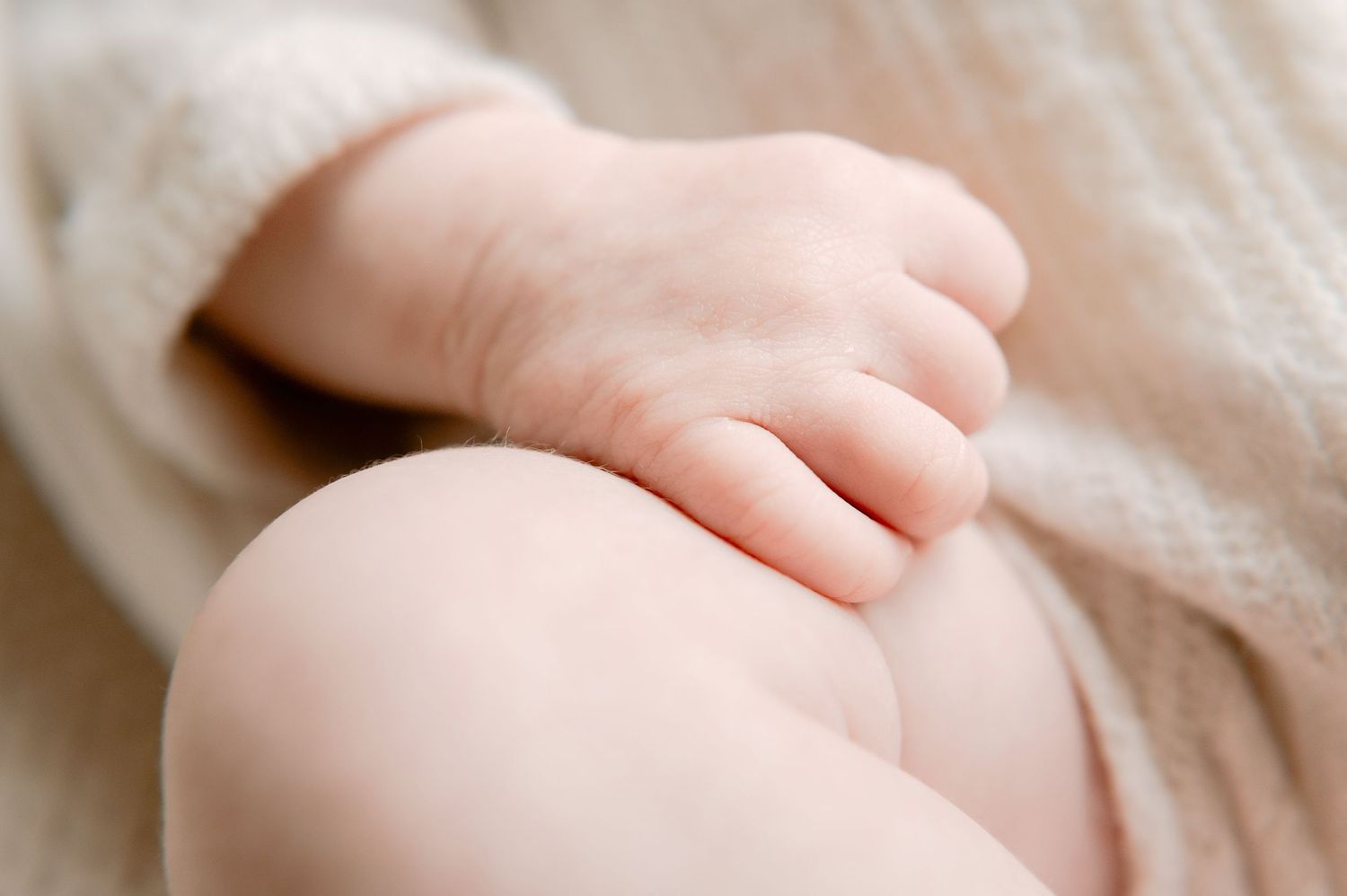 Close-up of a newborn baby's tiny hand resting gently on a soft beige knitted blanket.