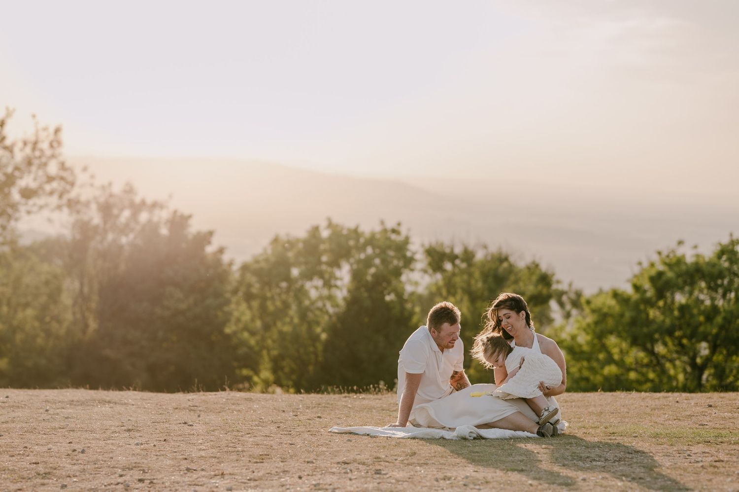 Couple sitting on hilltop at golden hour looking at newborn baby during outdoor family session.
