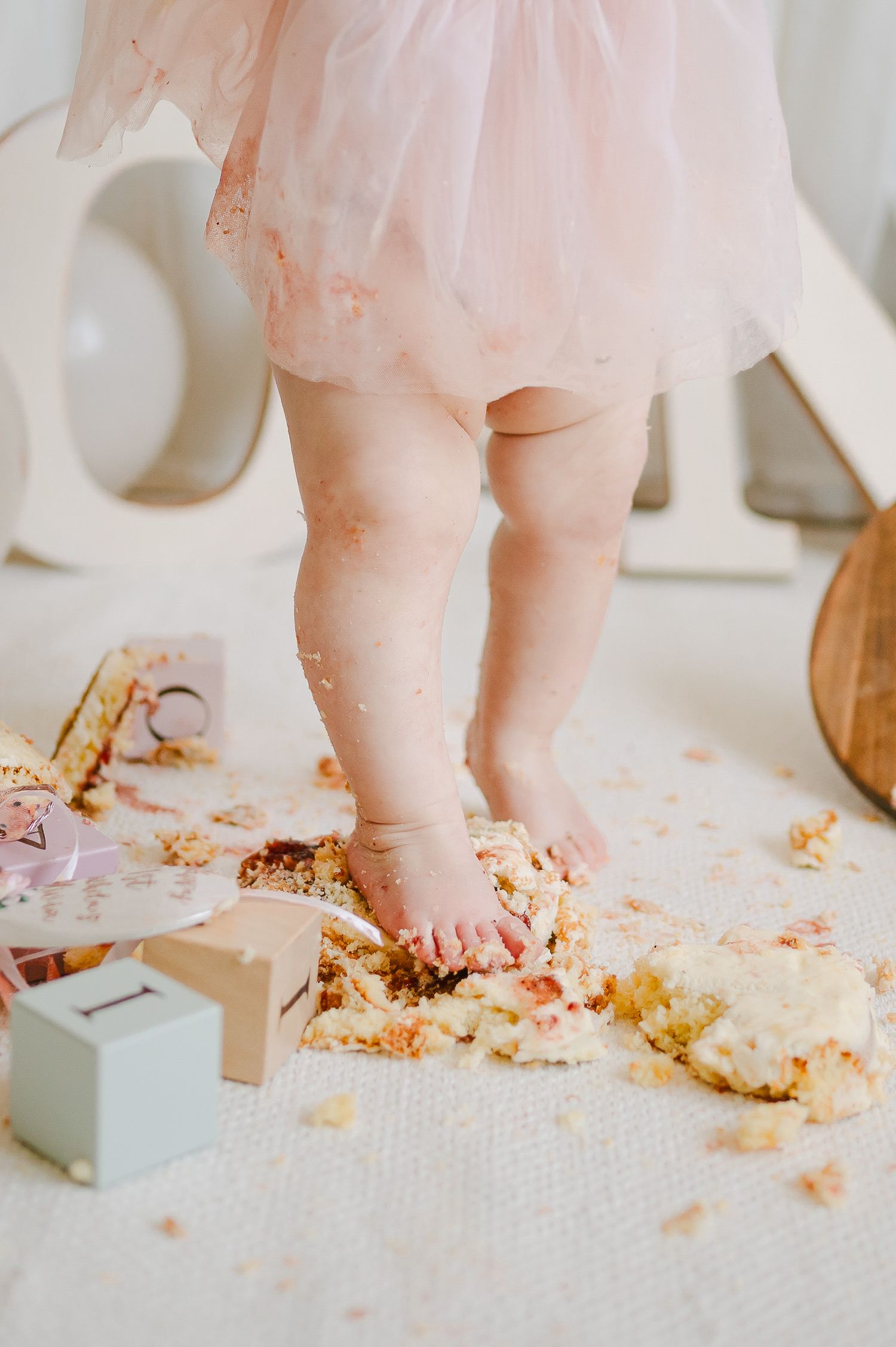 Baby girl in pink tutu standing in smashed birthday cake during first birthday cake smash.
