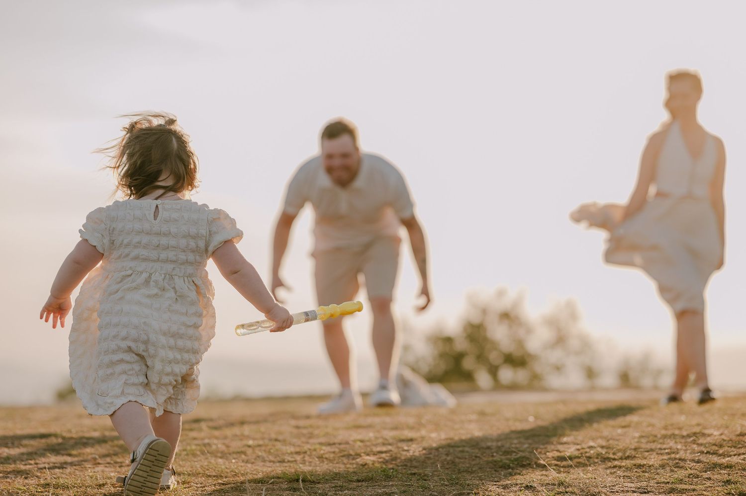 Young girl in white dress running toward her parents during a golden hour family photo session.
