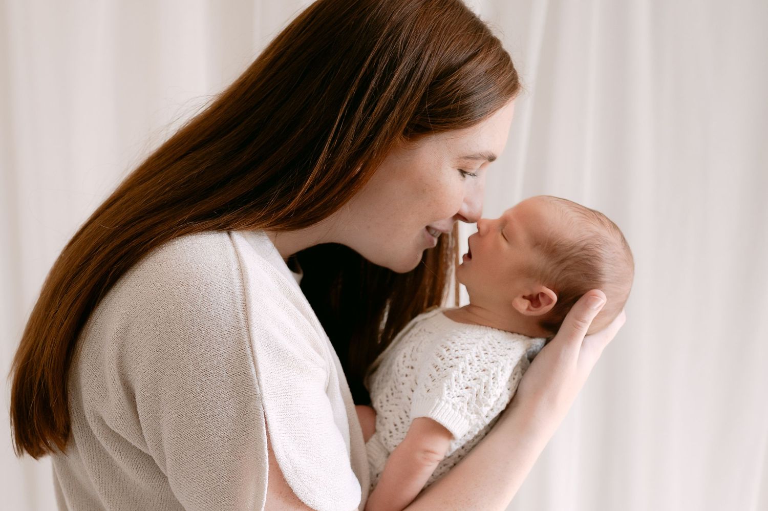 Loving mother holding her newborn baby close, touching noses in a tender moment.