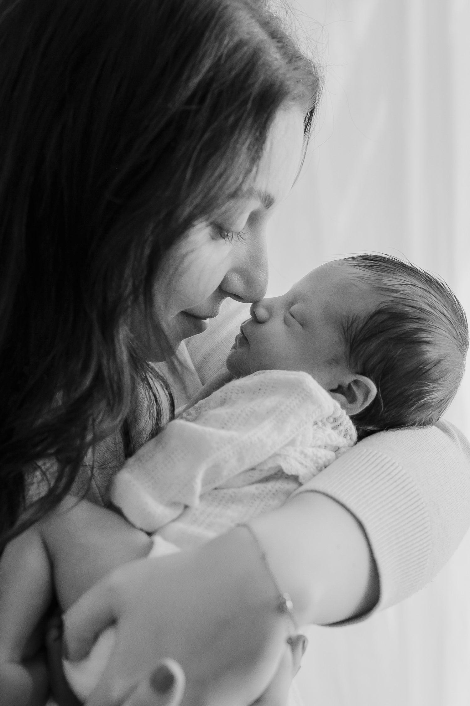 Black and white photo of mother tenderly touching noses with newborn baby.