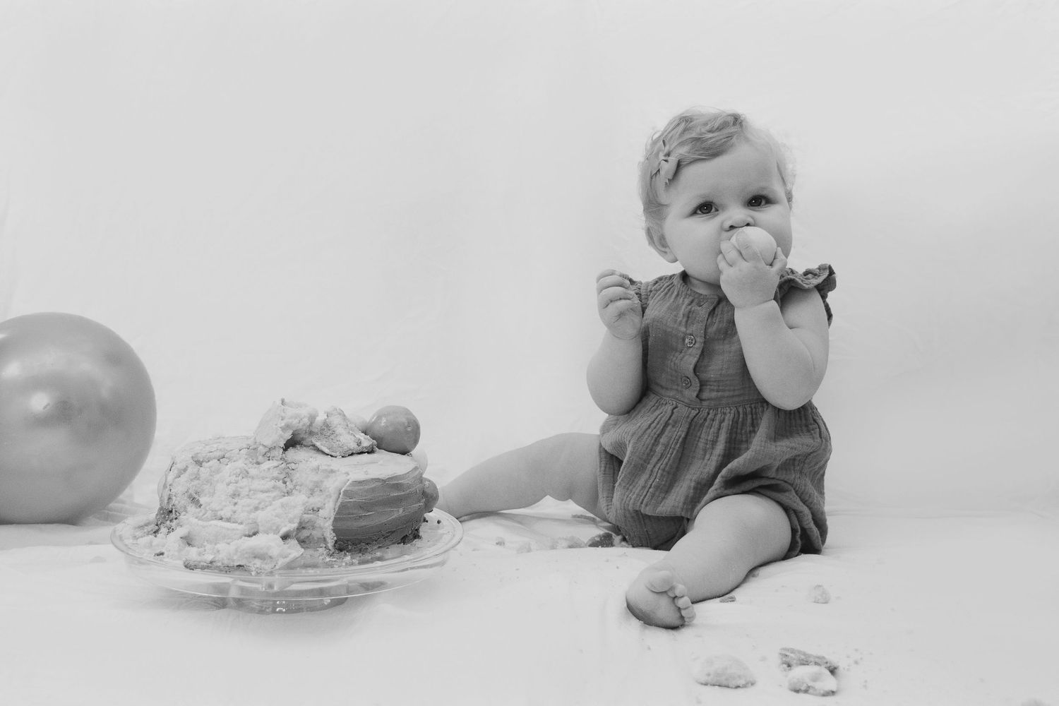 Black and white photo of baby girl sitting beside birthday cake during cake smash.